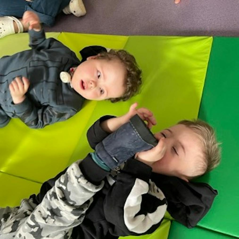 Two babies are lying on a green mat together