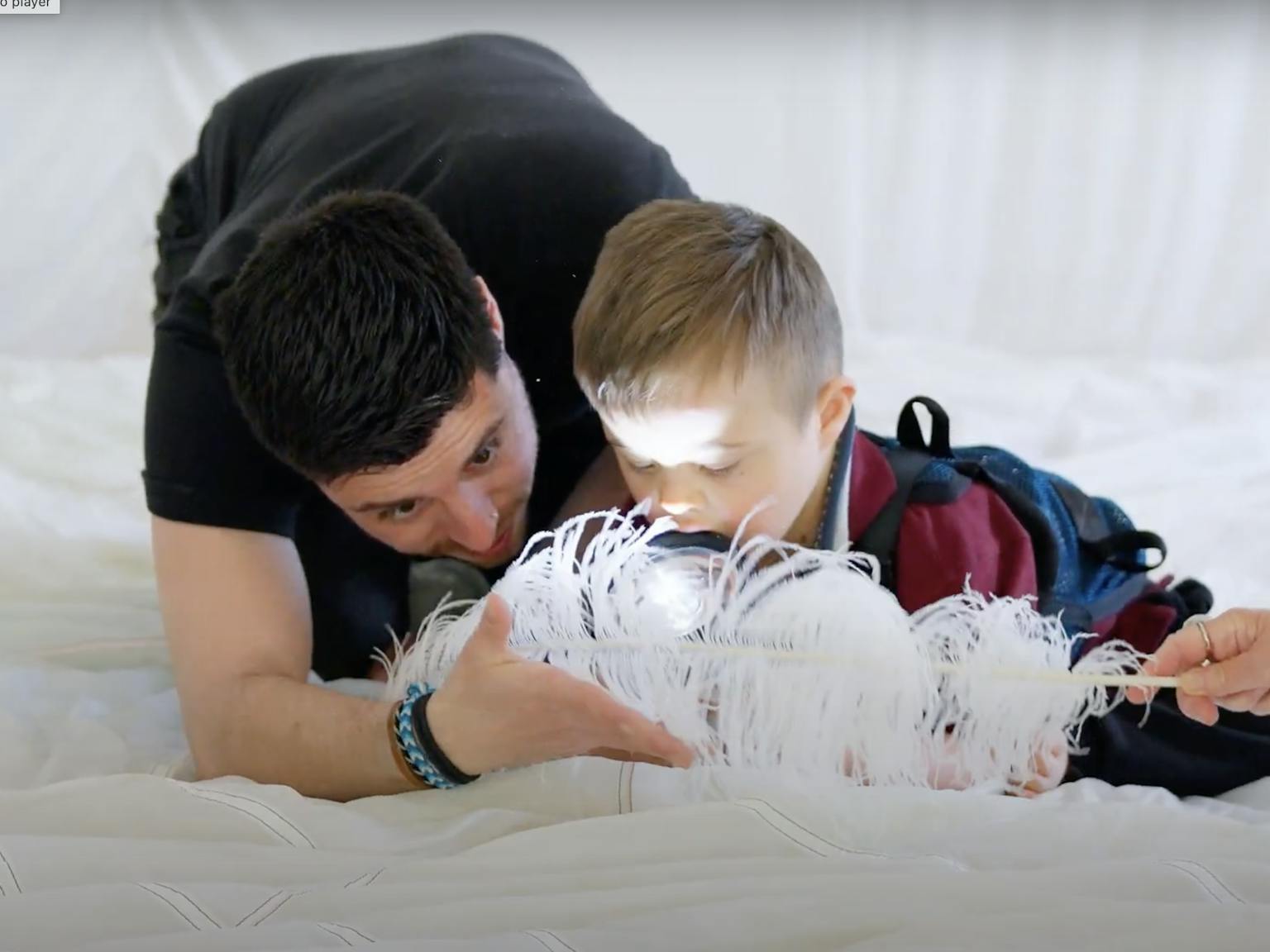 A young child and Playground artist are on a white piece of material together. They are playing with a feather and torch.