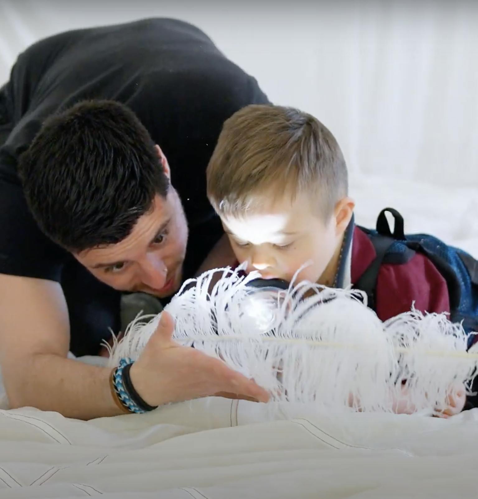 A young child and Playground artist are on a white piece of material together. They are playing with a feather and torch.