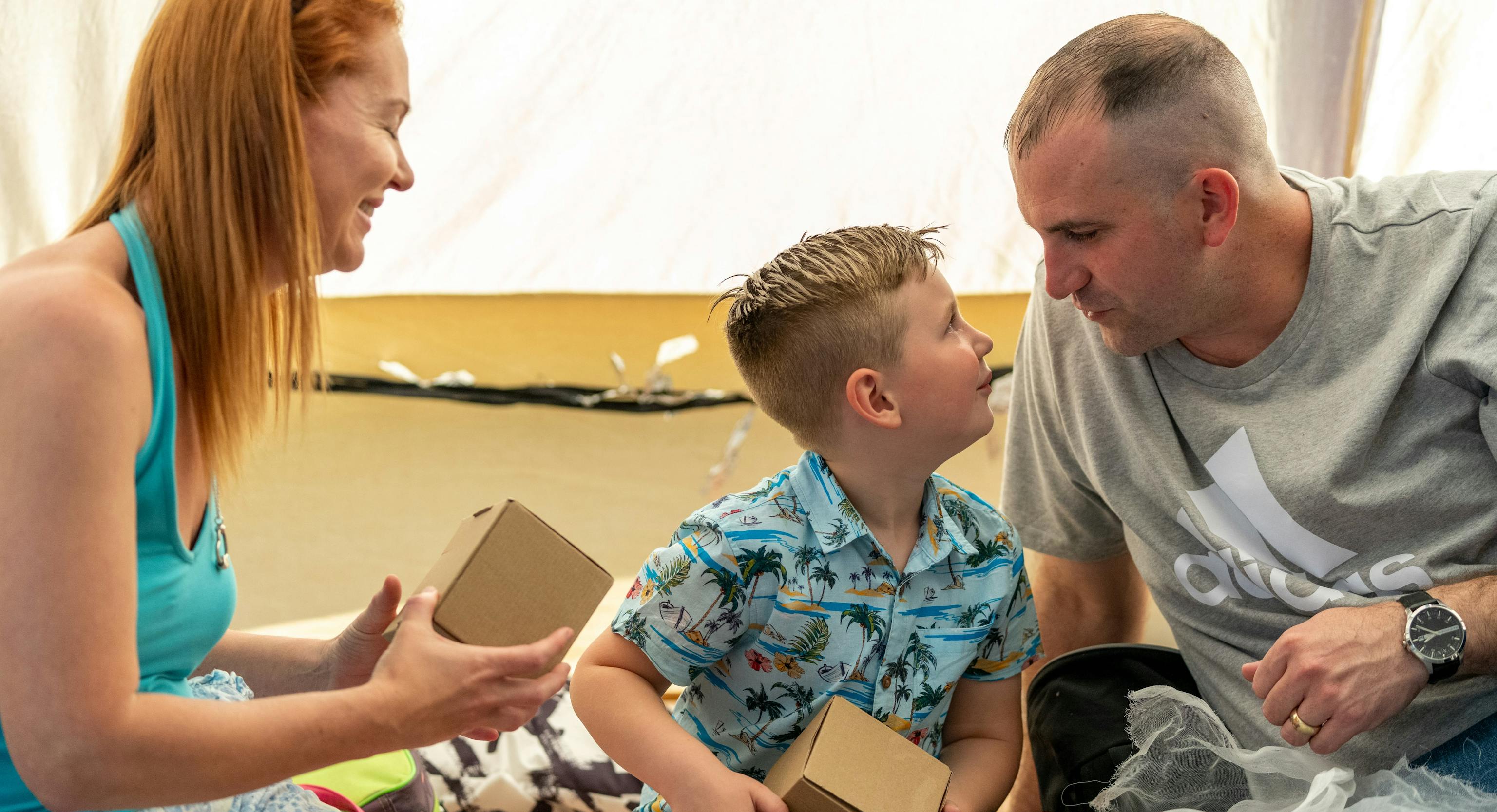 A young child sat in-between their parent/carers. They are holding boxes and looking at each other