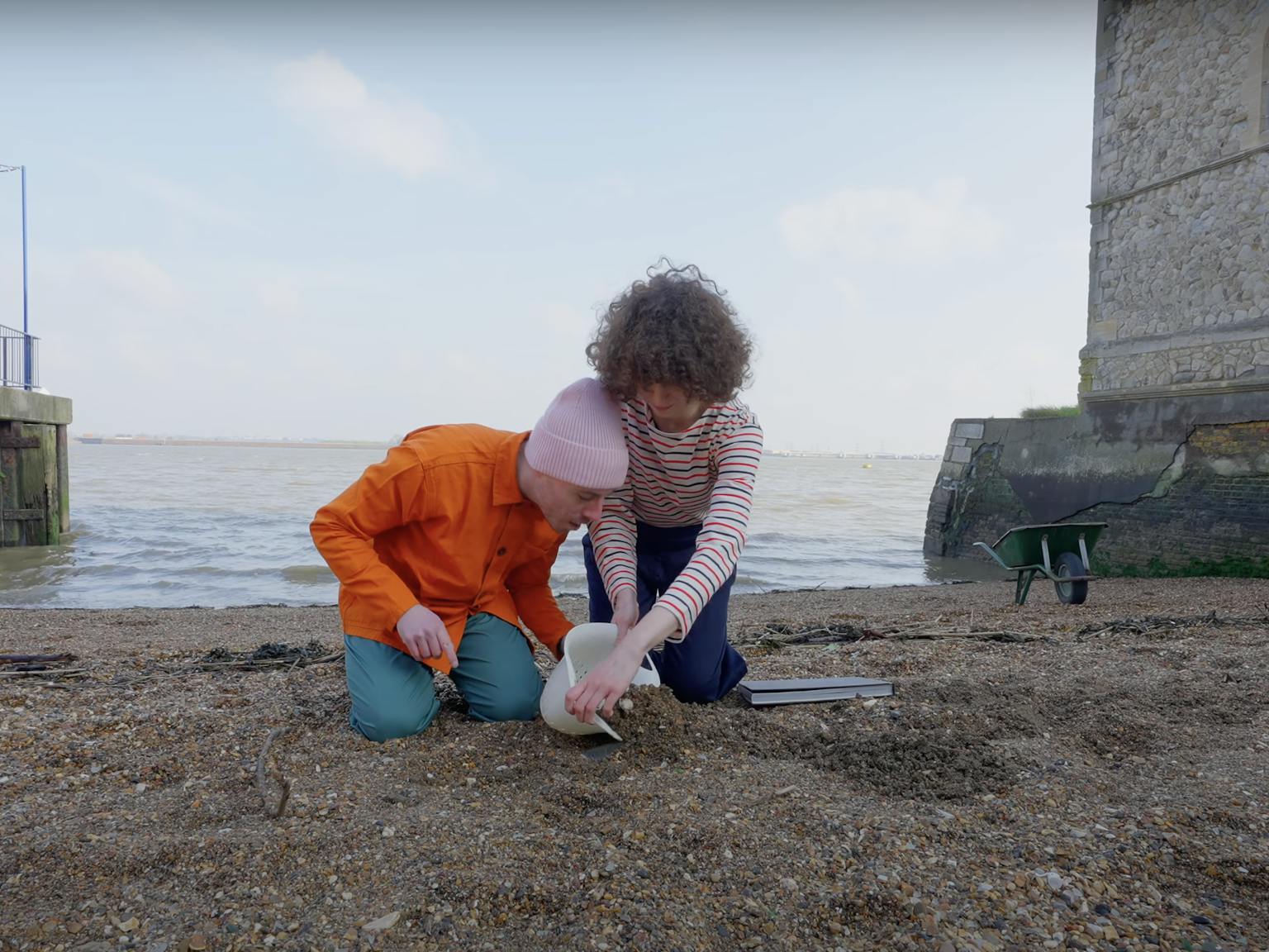 Two people on the beach. They are using a colander to dig up the sand to see what they will uncover