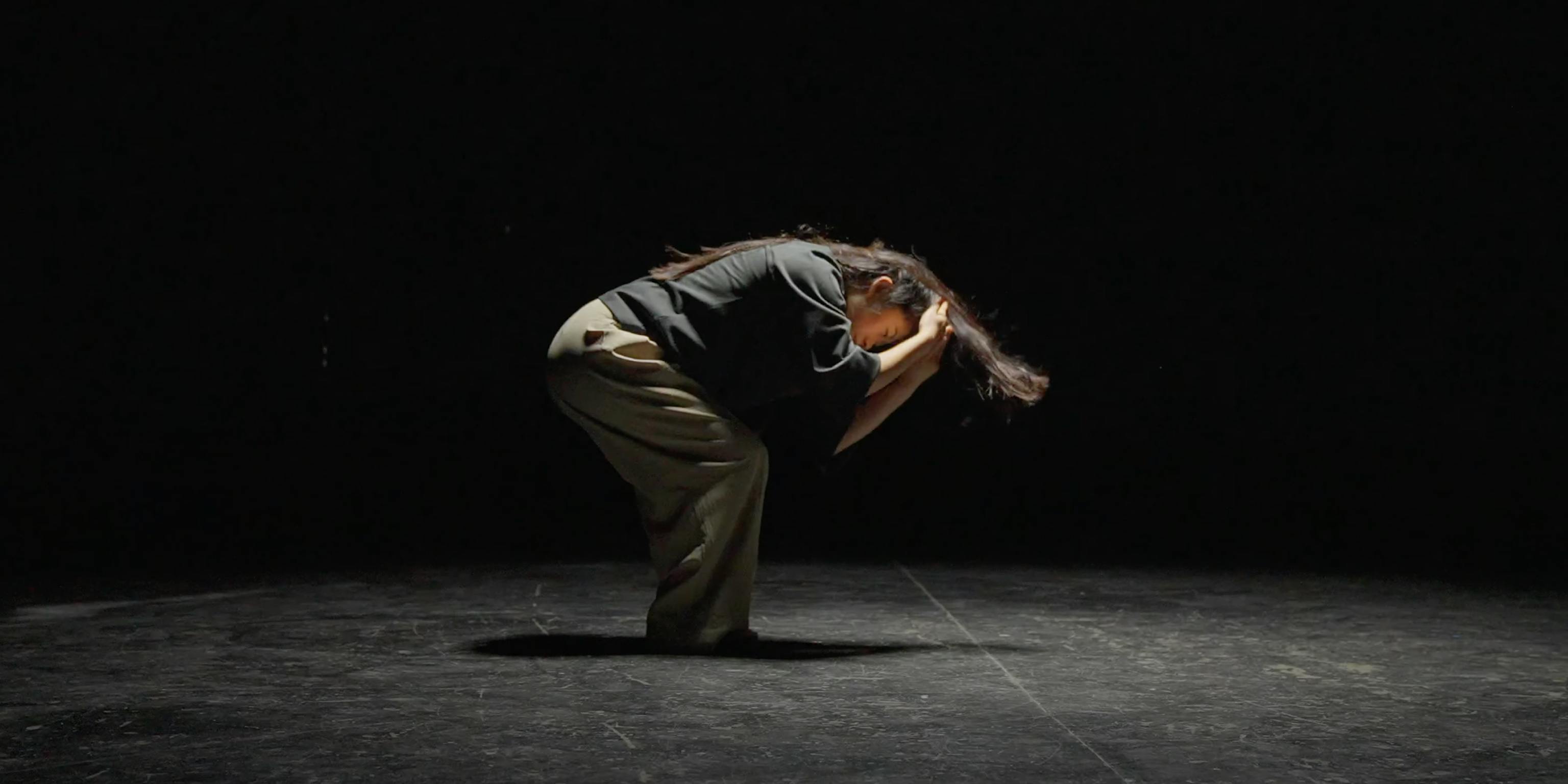 A dancer in a dark room, crouching in the middle of a routine