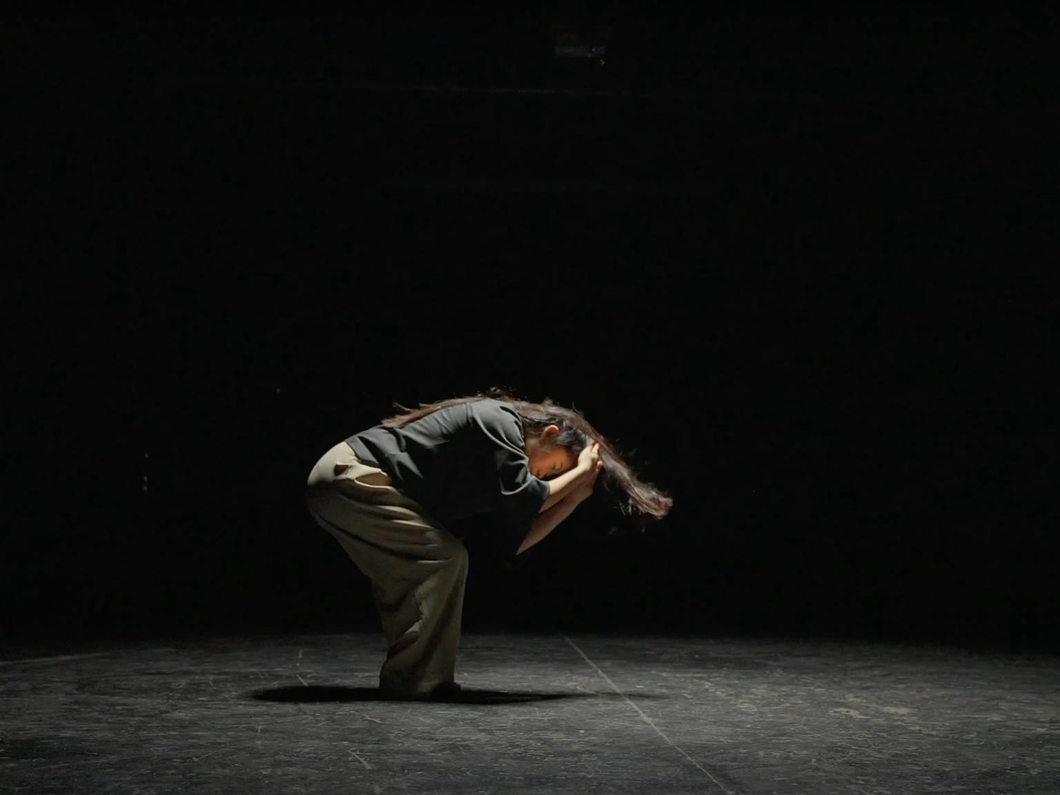A dancer in a dark room, crouching in the middle of a routine