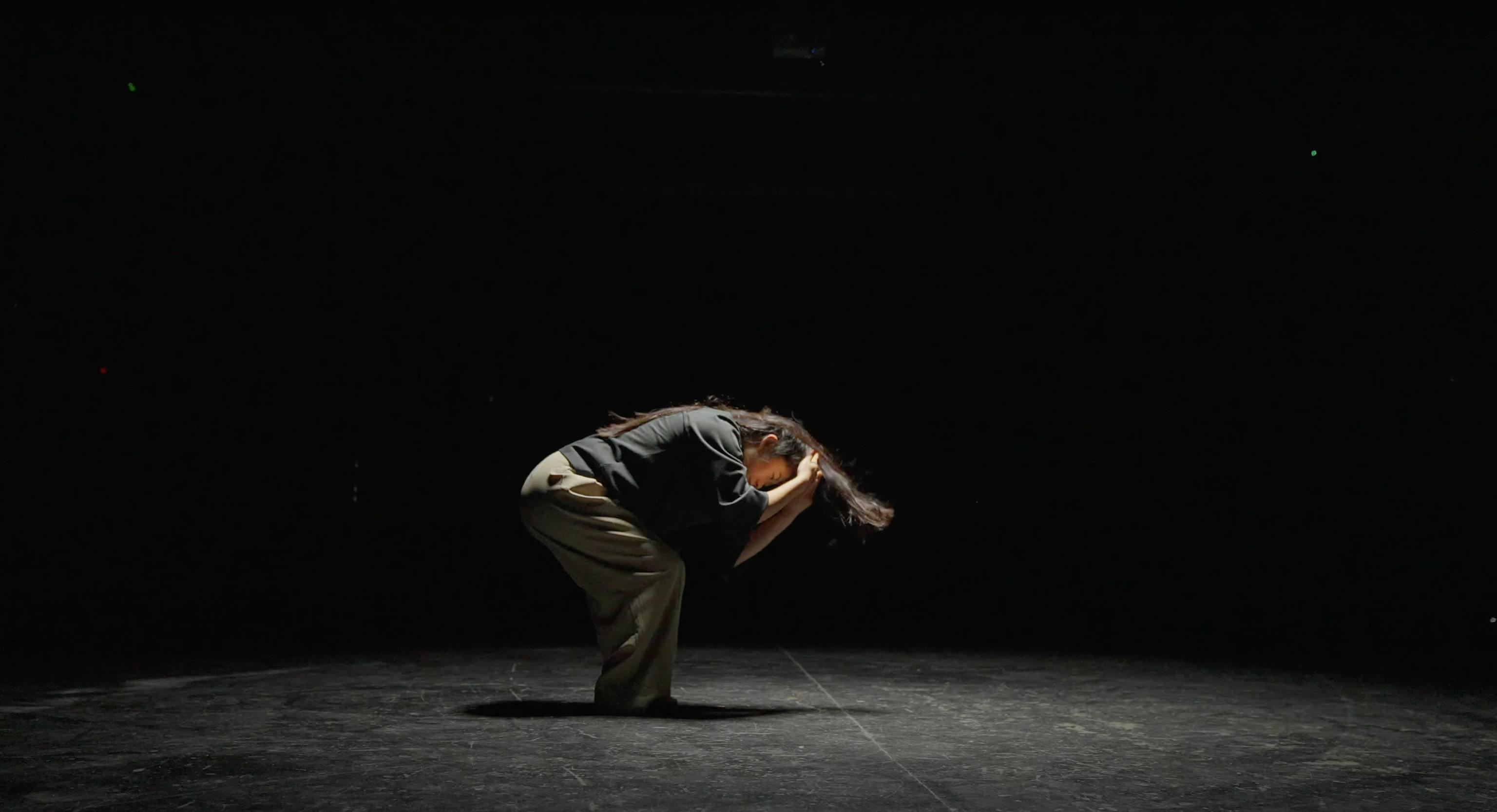 A dancer in a dark room, crouching in the middle of a routine