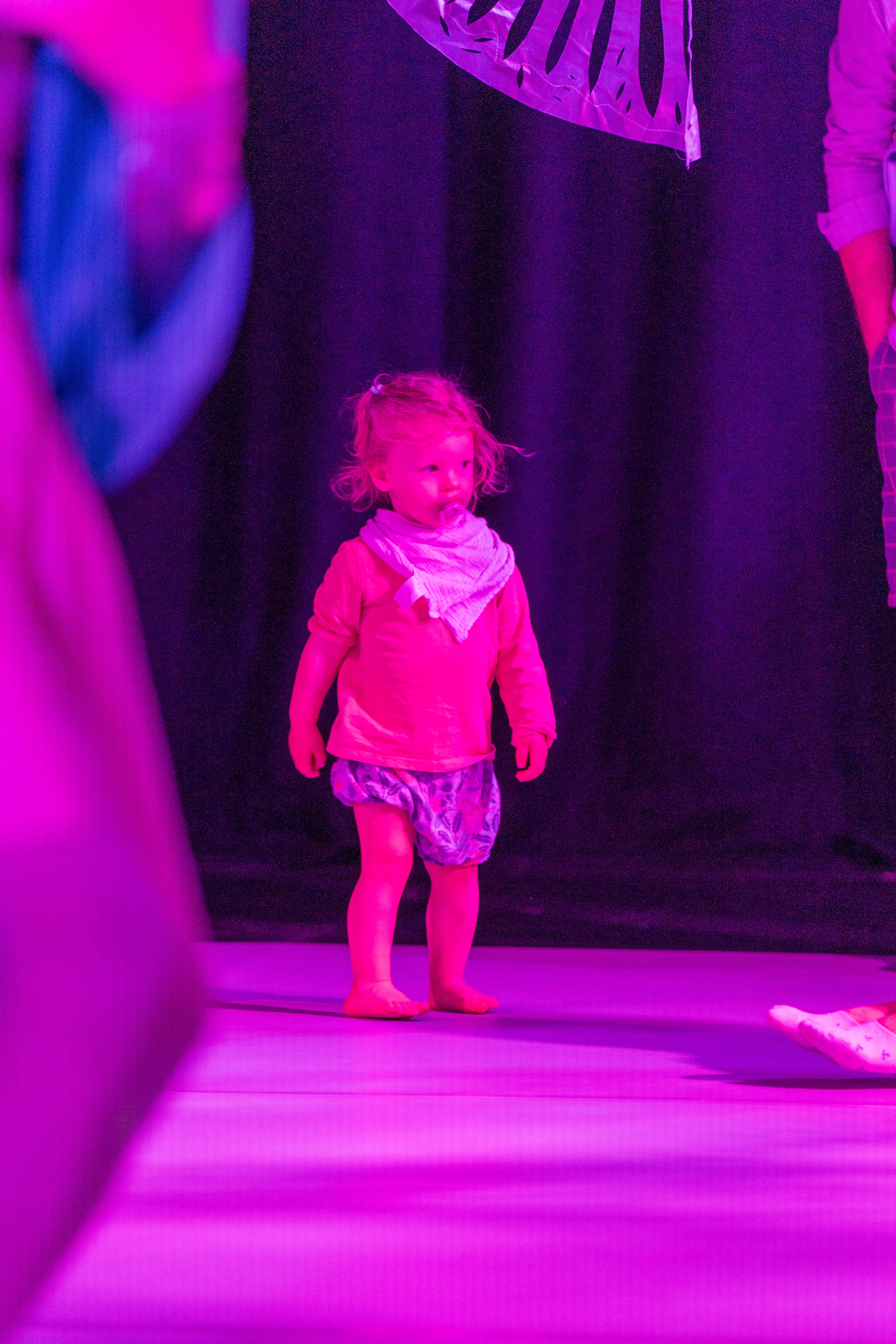 A young child in a pink lit performance space 