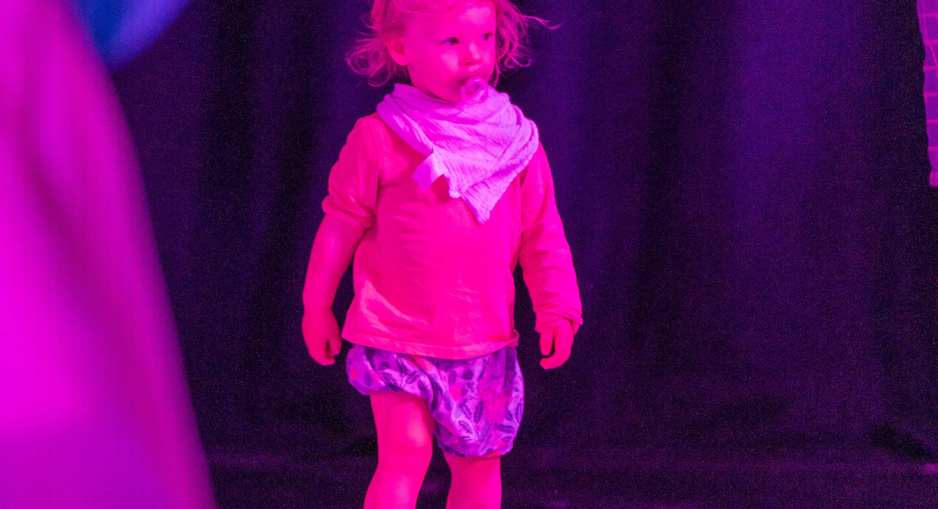 A young child in a pink lit performance space