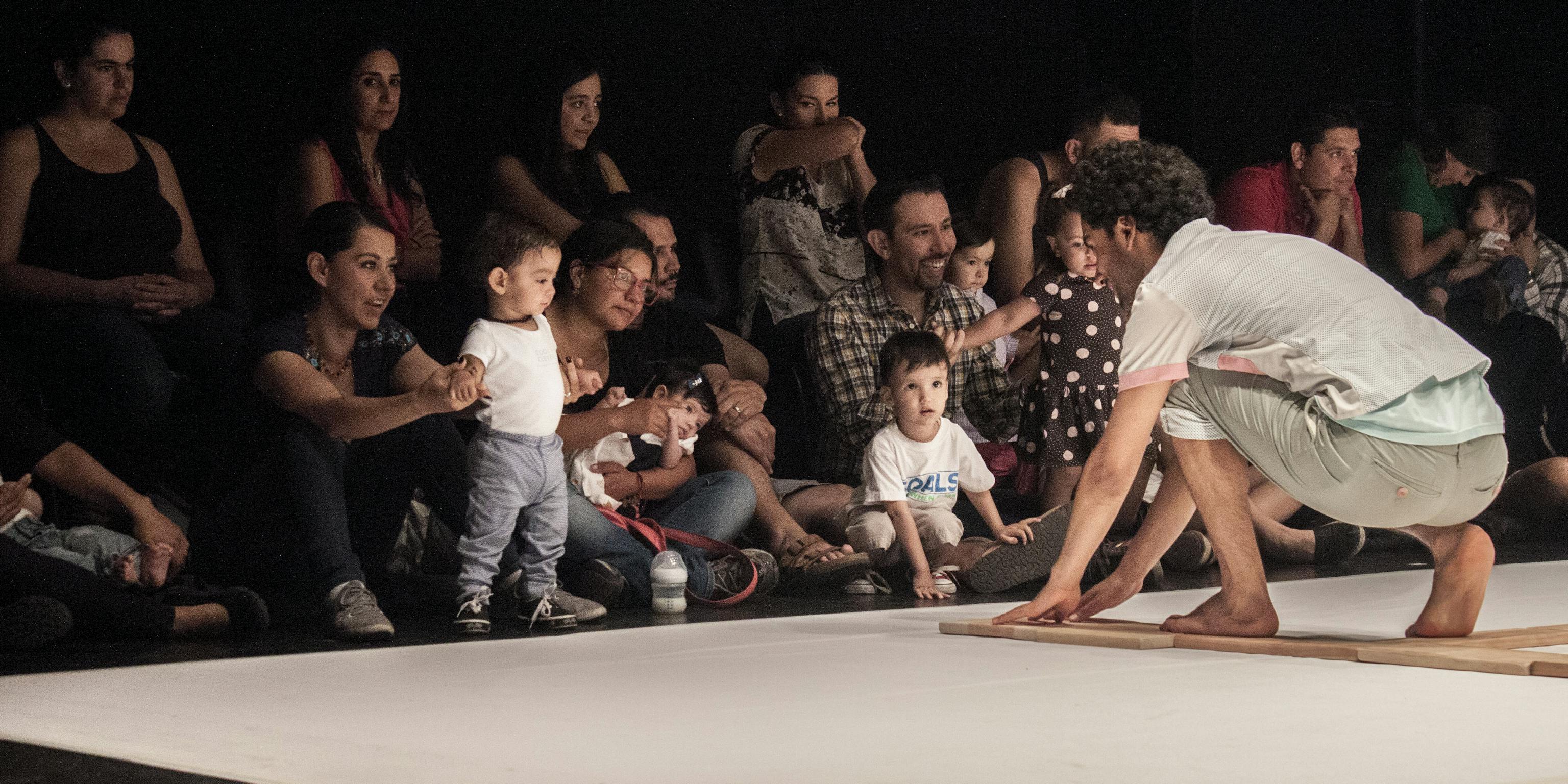An artist on stage engaging with a group of children and their parents/carers