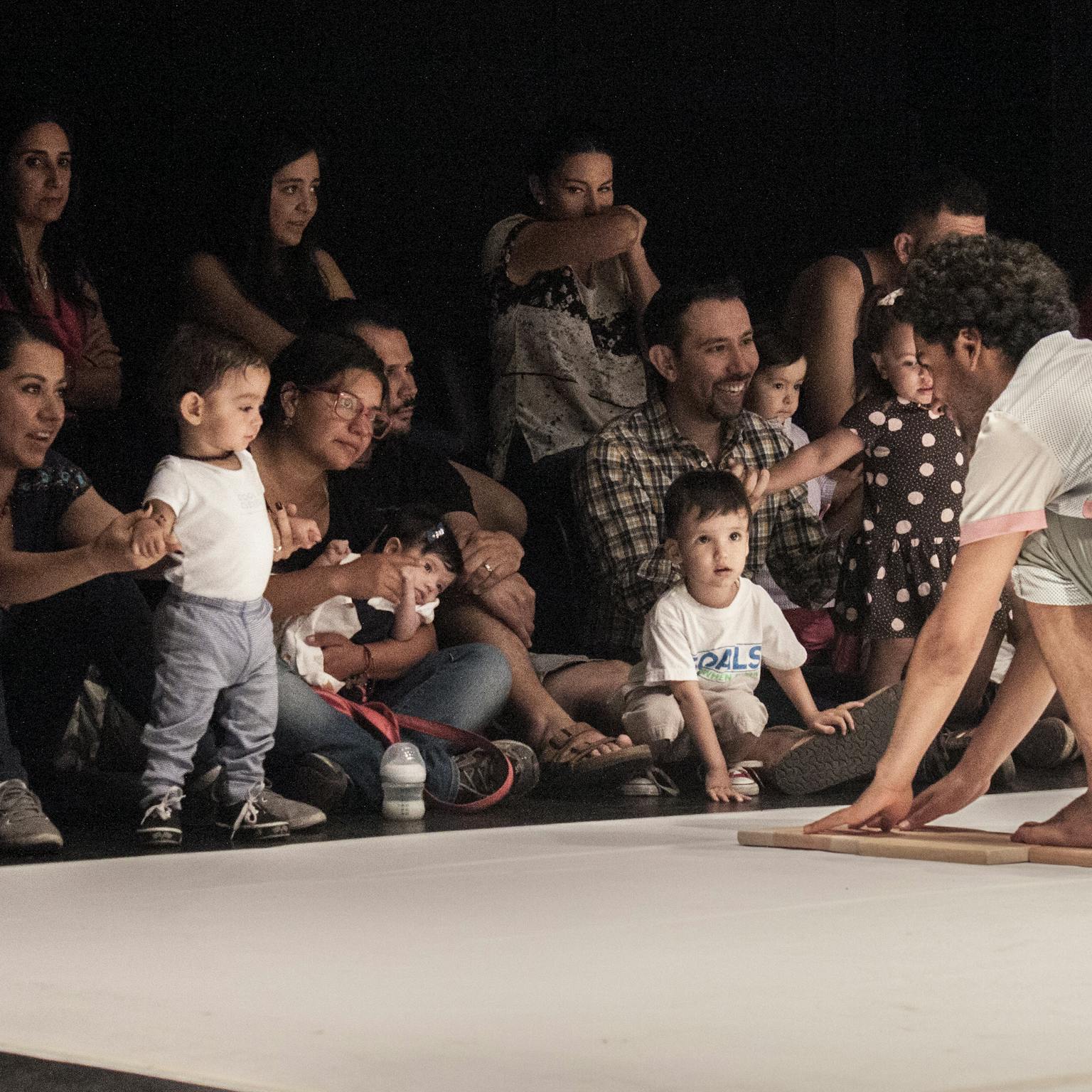 An artist on stage engaging with a group of children and their parents/carers
