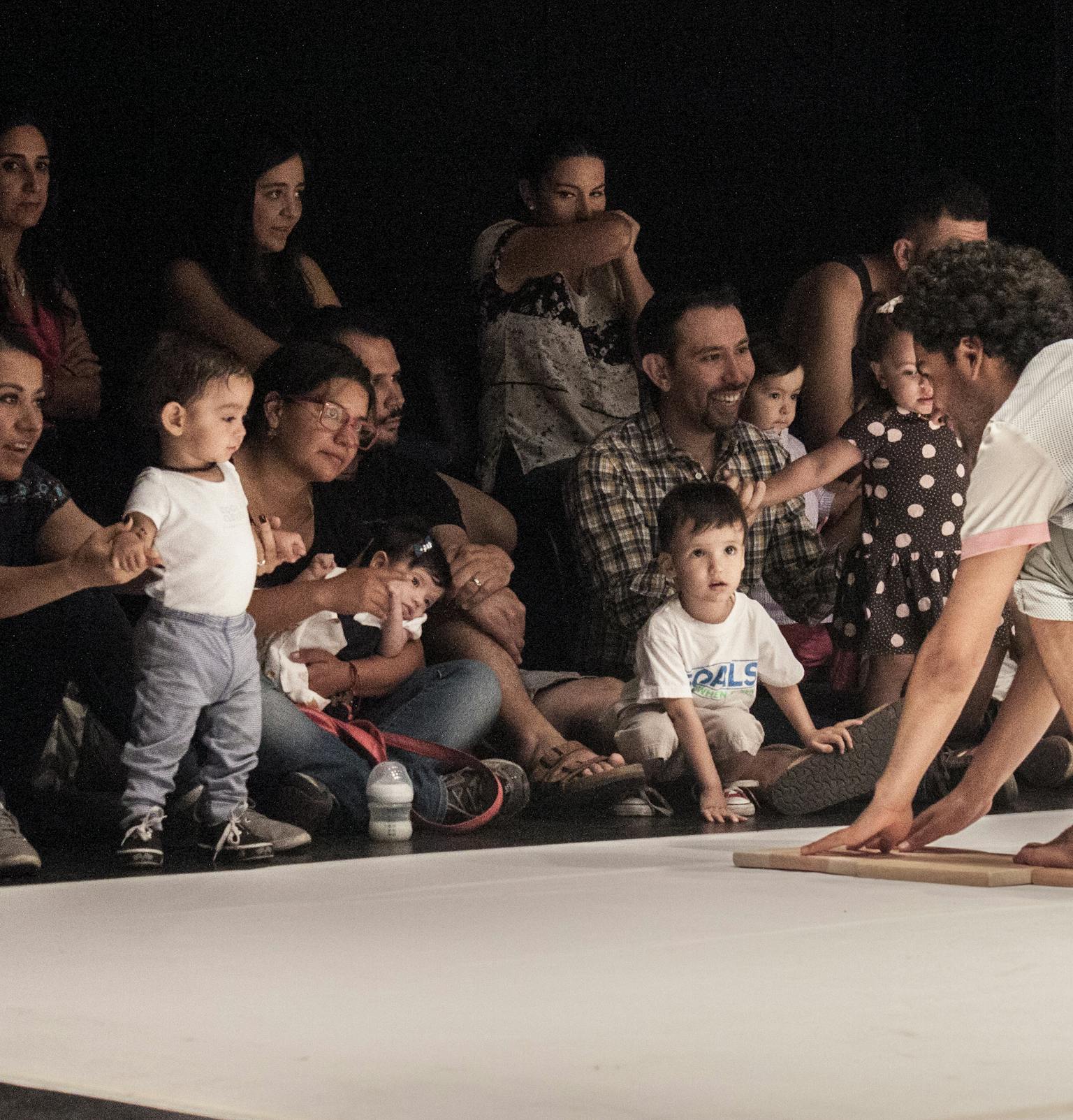 An artist on stage engaging with a group of children and their parents/carers