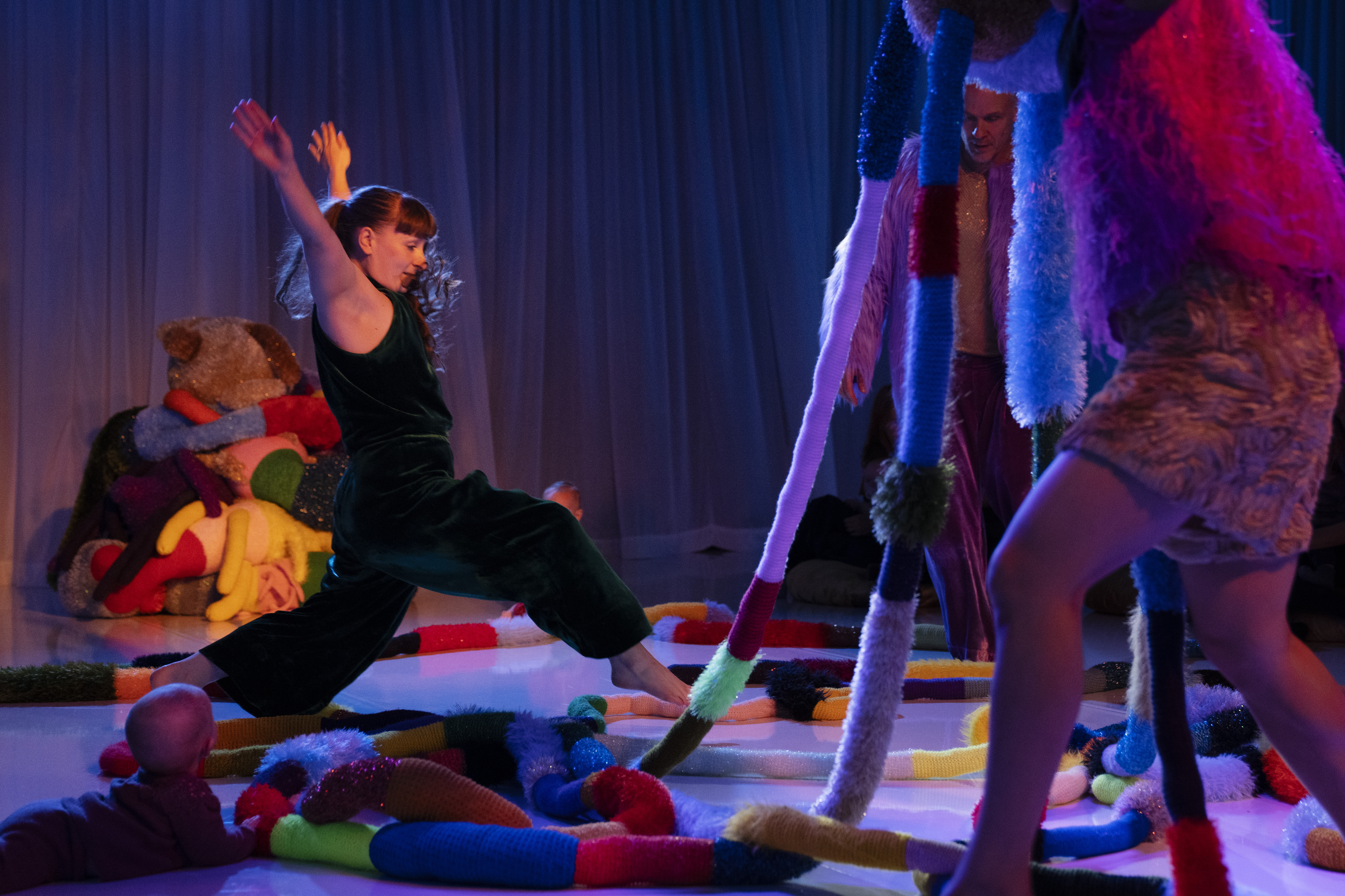 A performer in a darkly lit room is taking a leap over lots of textured materials. they are surrounded by a lot of different shapes and textures 