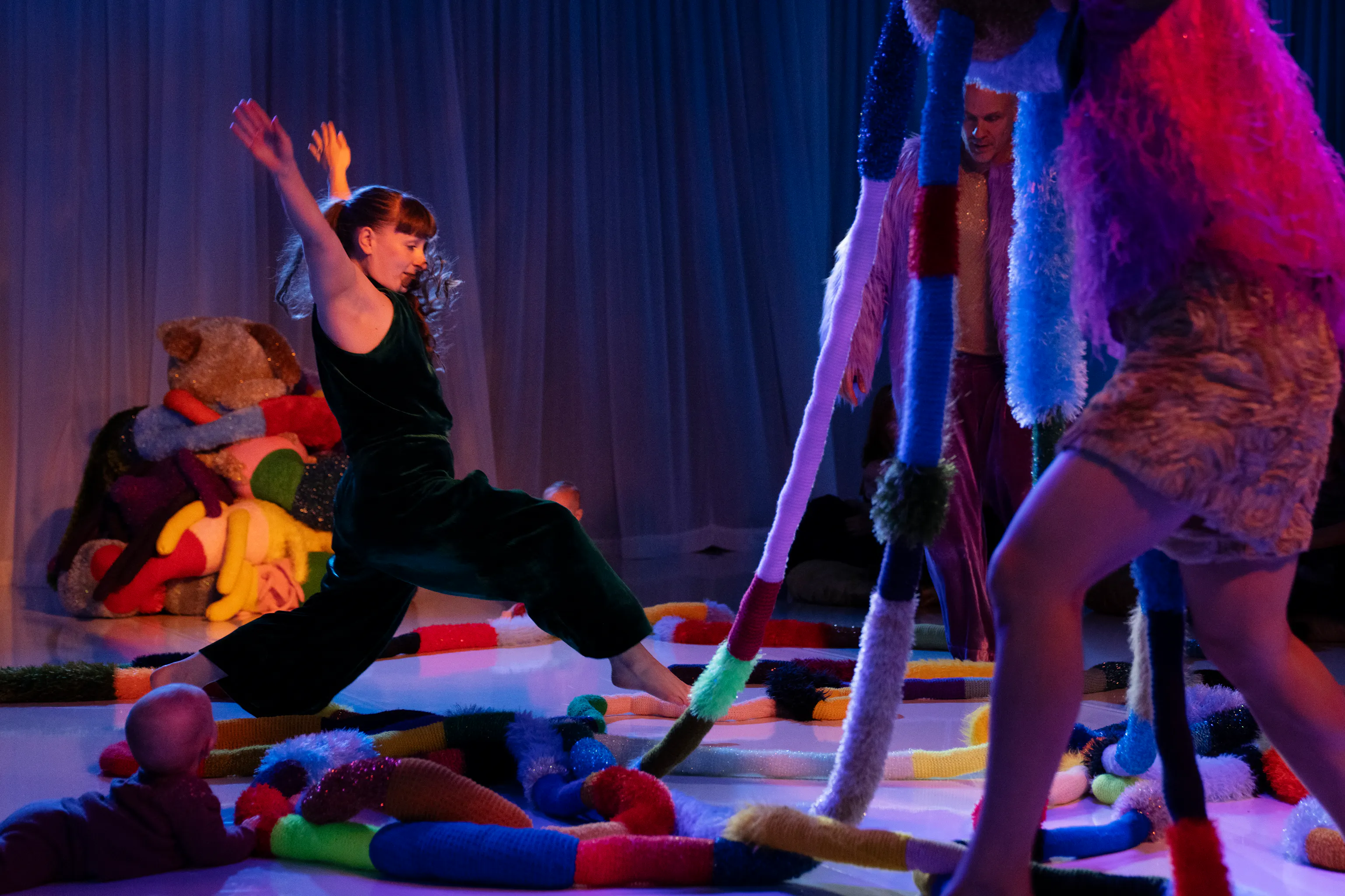 A performer in a darkly lit room is taking a leap over lots of textured materials. they are surrounded by a lot of different shapes and textures