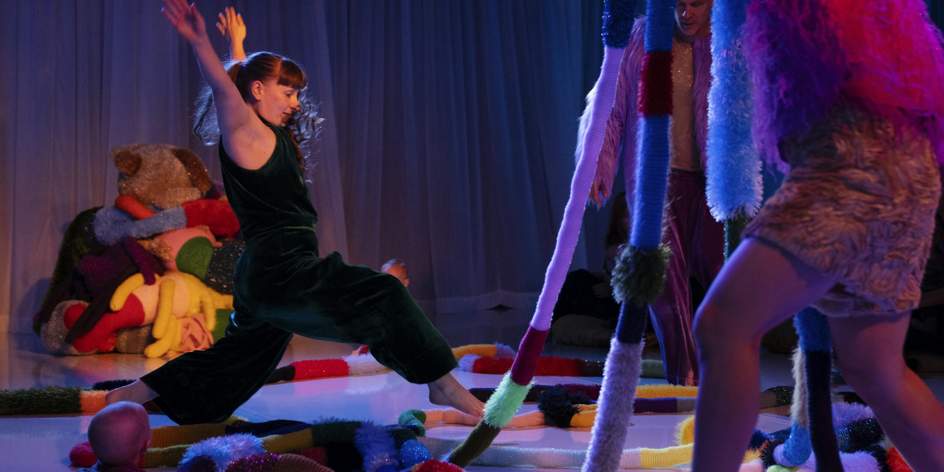 A performer in a darkly lit room is taking a leap over lots of textured materials. they are surrounded by a lot of different shapes and textures