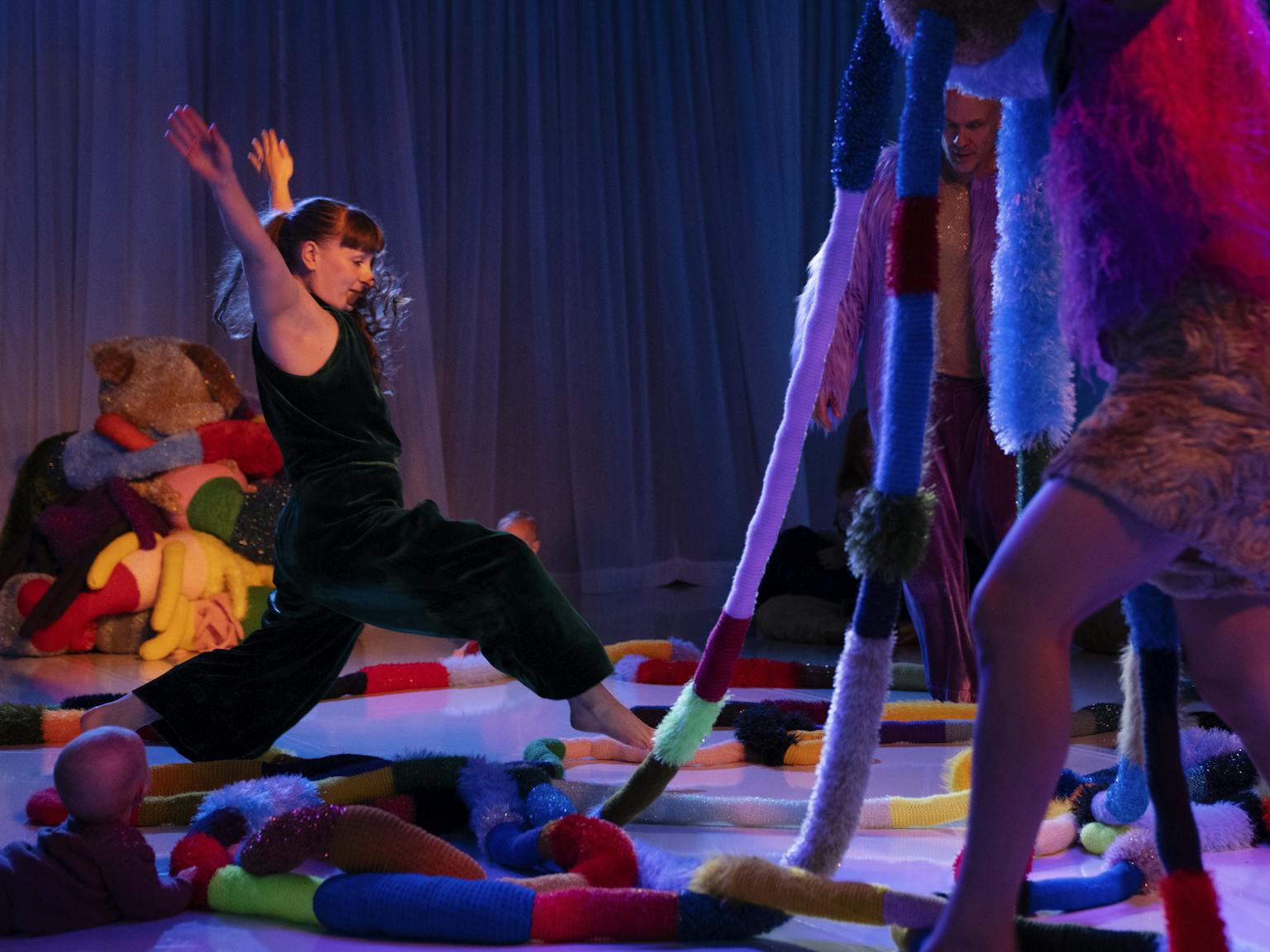 A performer in a darkly lit room is taking a leap over lots of textured materials. they are surrounded by a lot of different shapes and textures