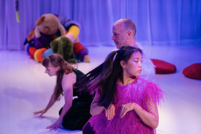 A group of performers looking in different directions. Behind them is a big, colourful and textured share 