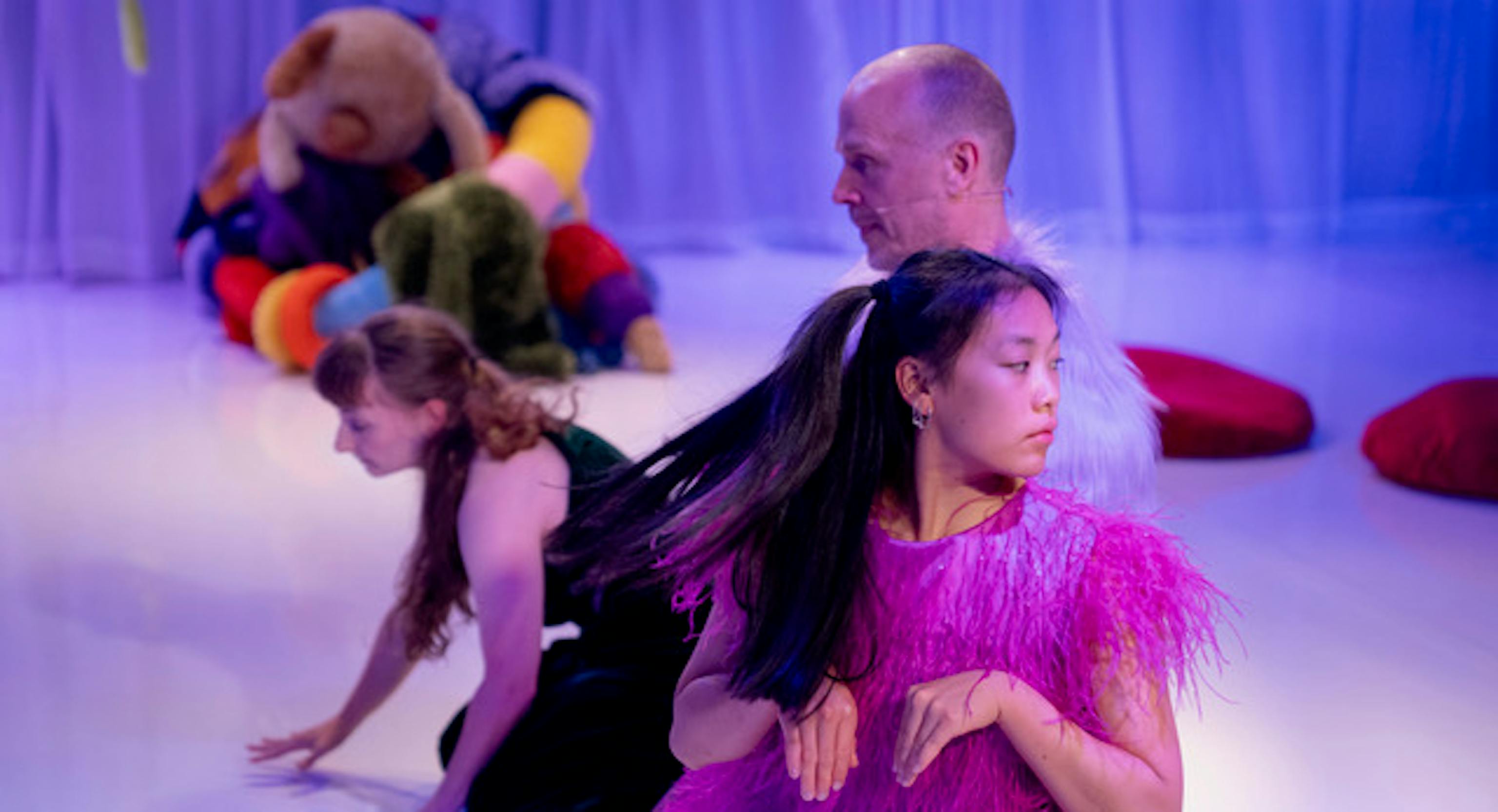 A group of performers looking in different directions. Behind them is a big, colourful and textured share