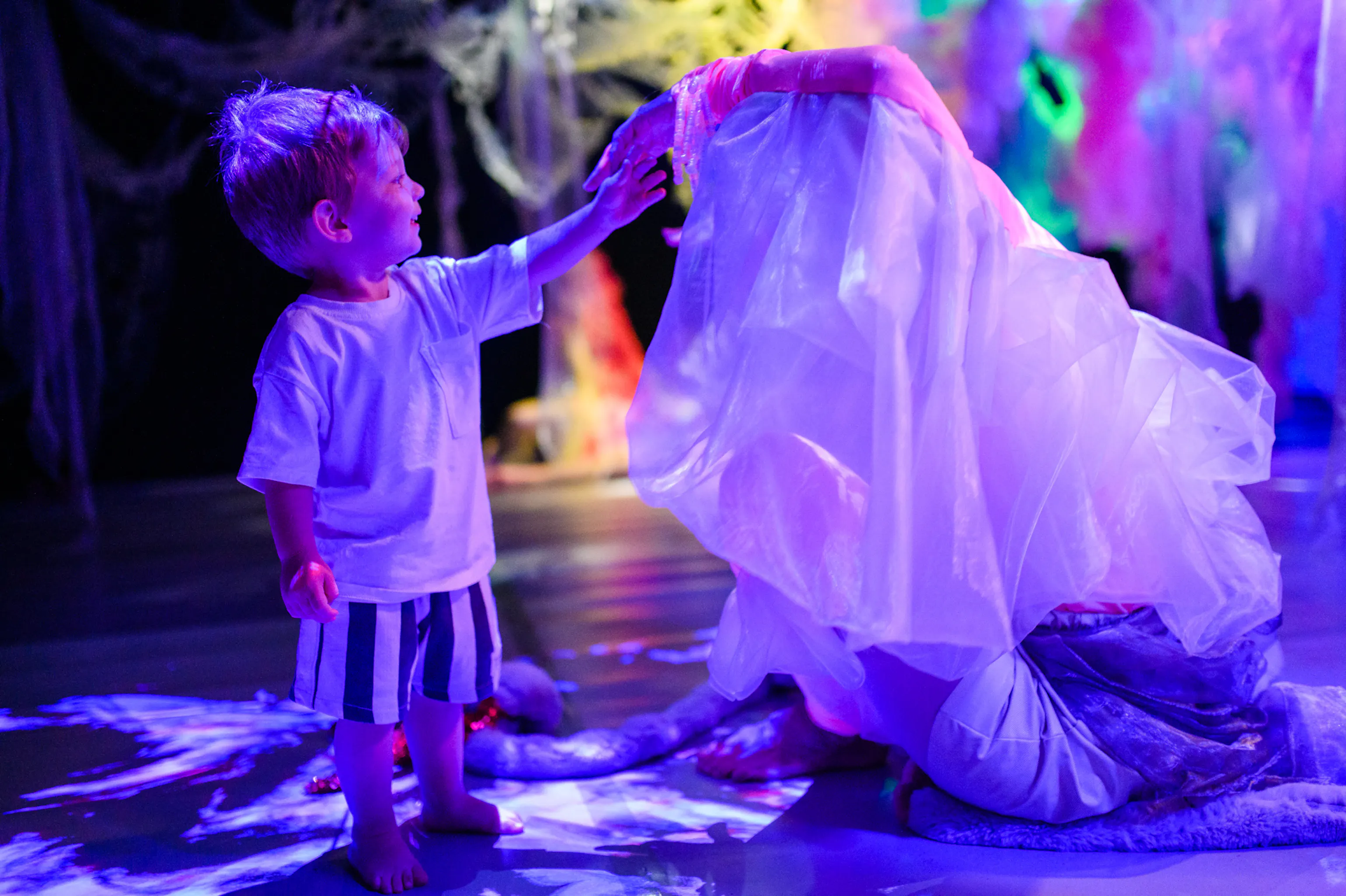A young child standing and touching the performers veil who is sat down