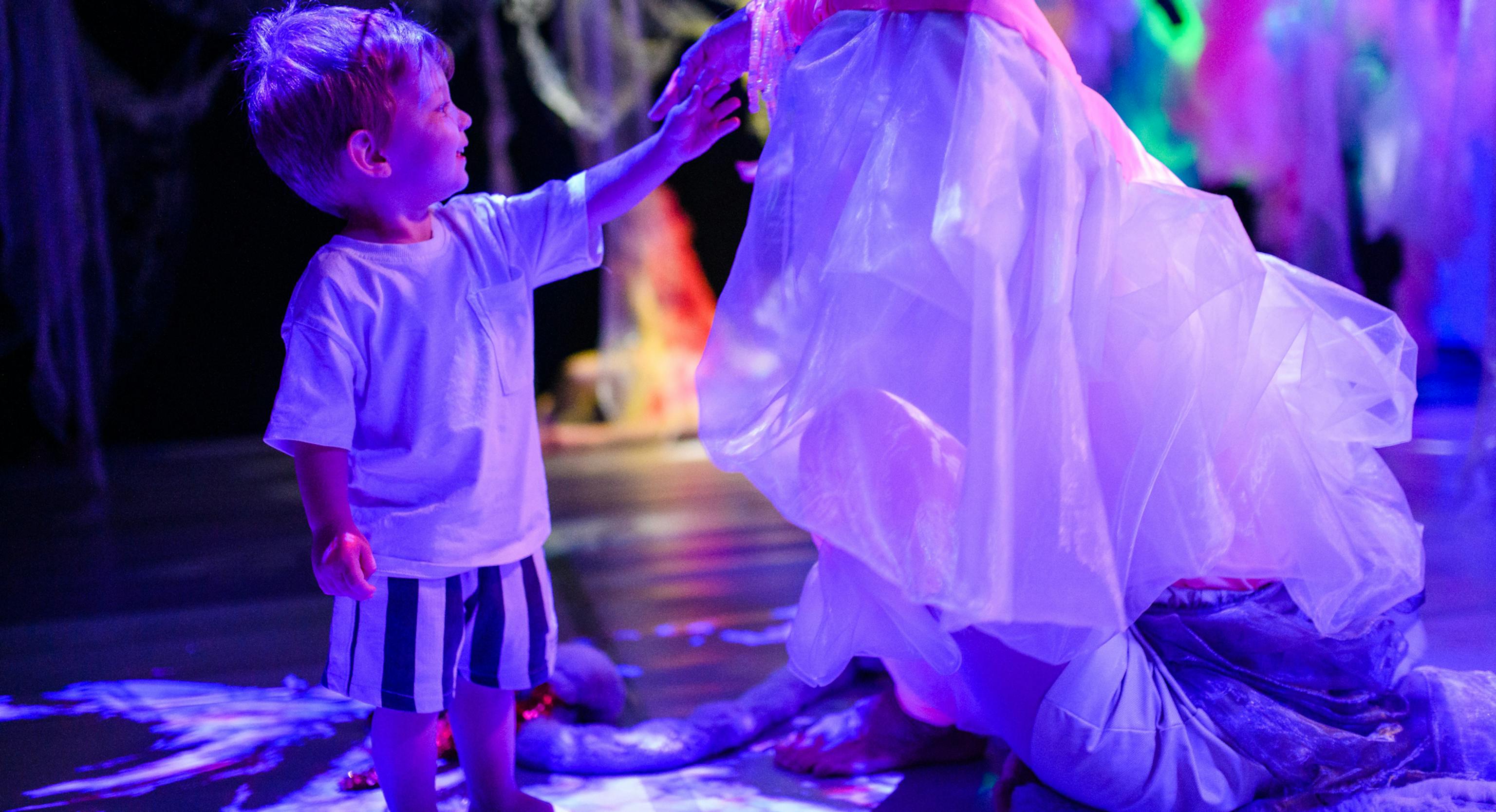 A young child standing and touching the performers veil who is sat down