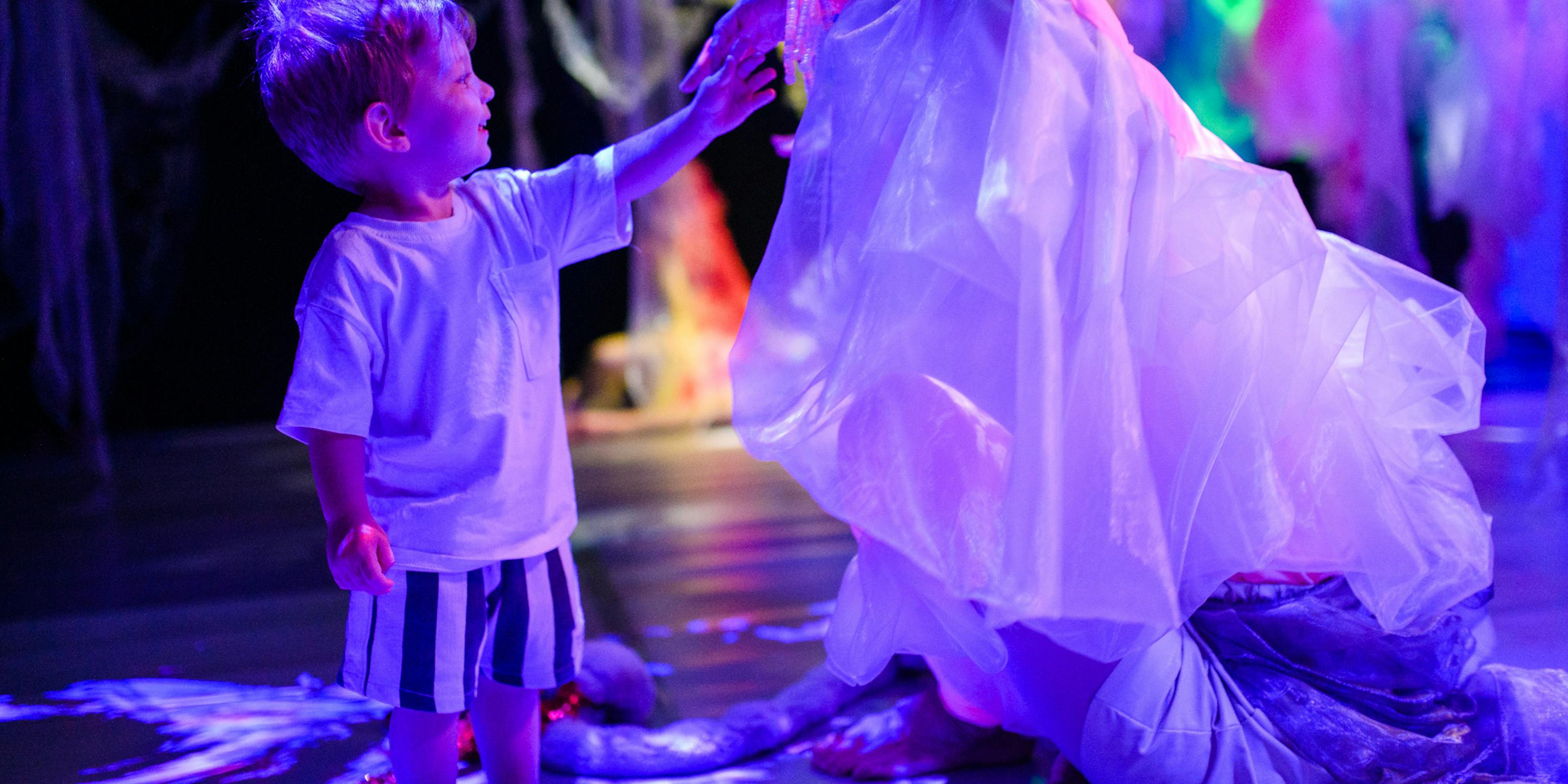 A young child standing and touching the performers veil who is sat down