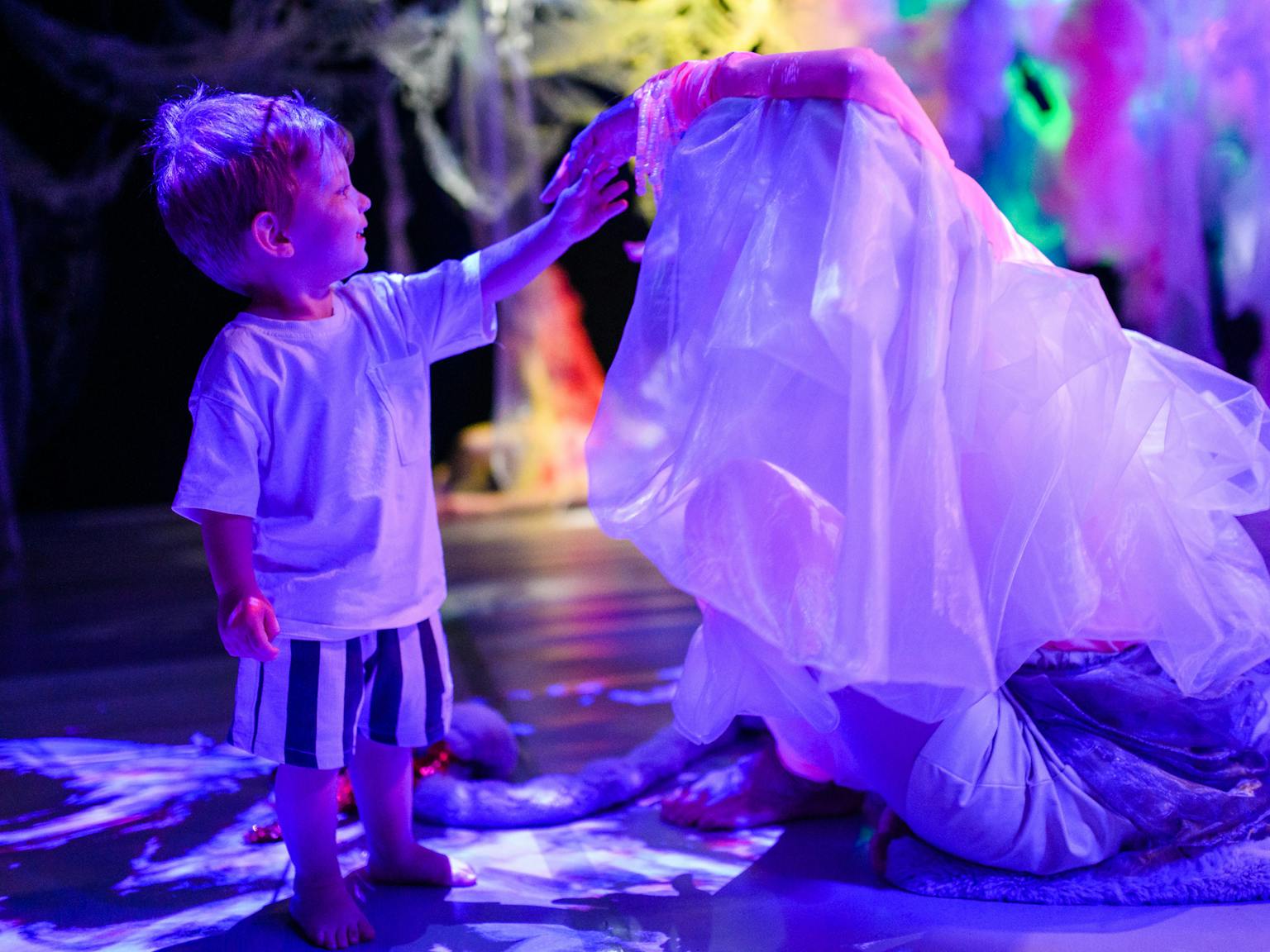 A young child standing and touching the performers veil who is sat down