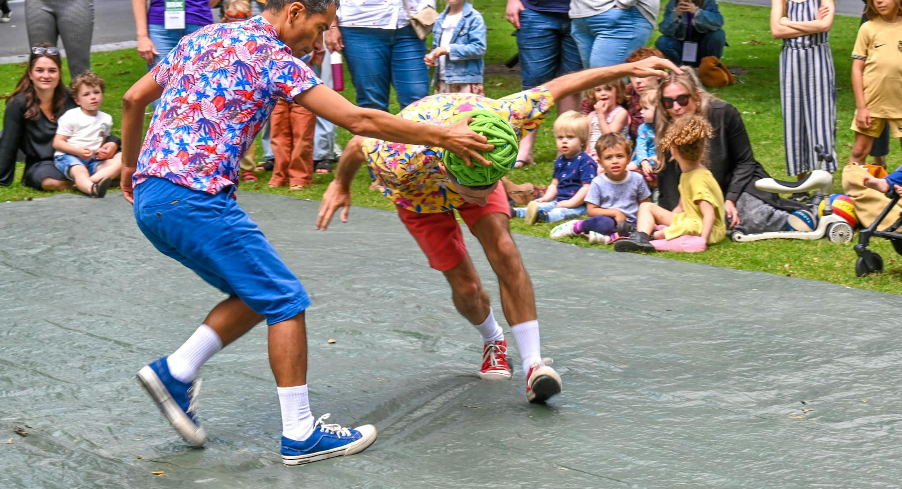Two performers during a performance. Once is holding a ball of rope over the other's head