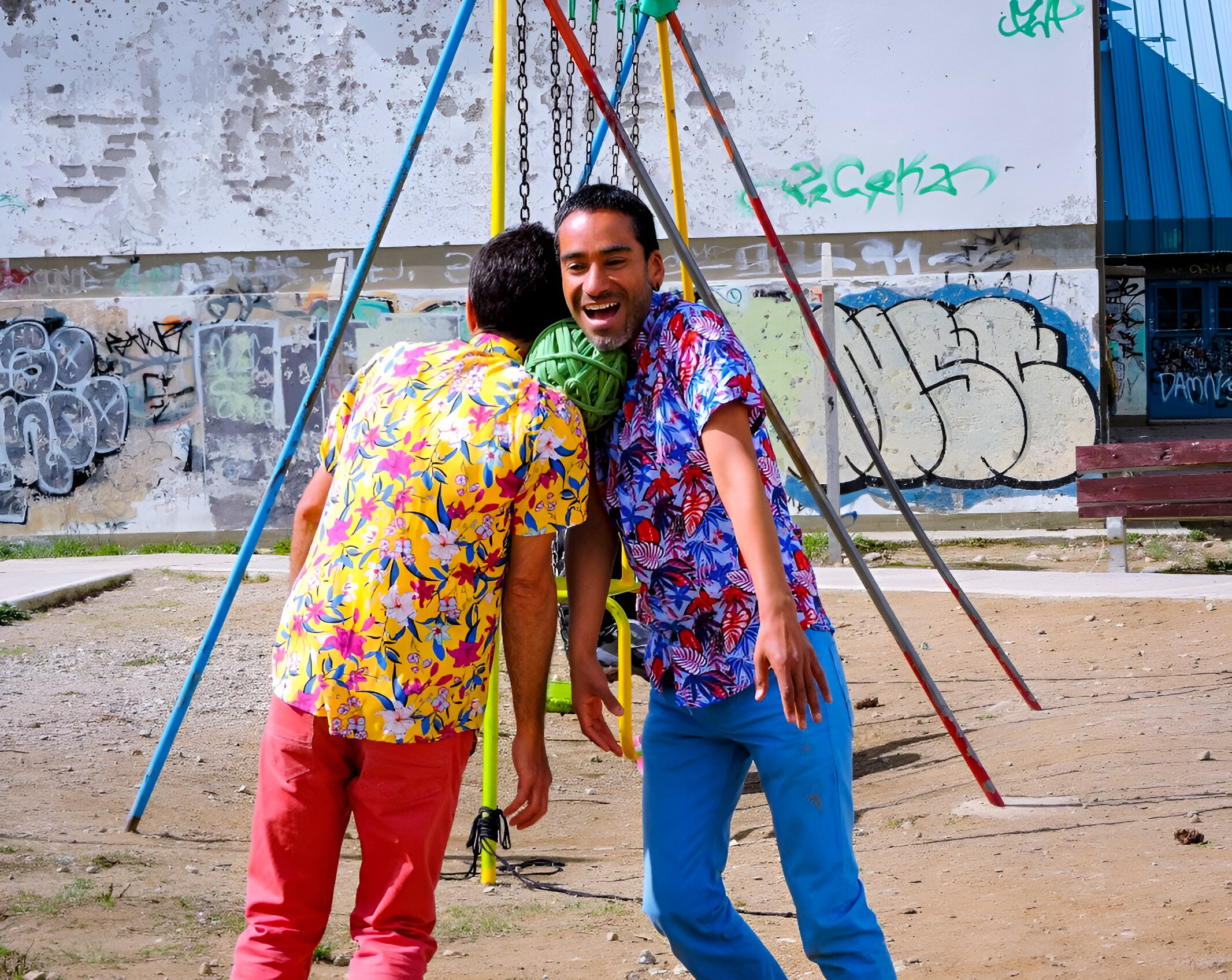 Two performers wearing colourful shirts are holding a ball of rope between with their shoulders 