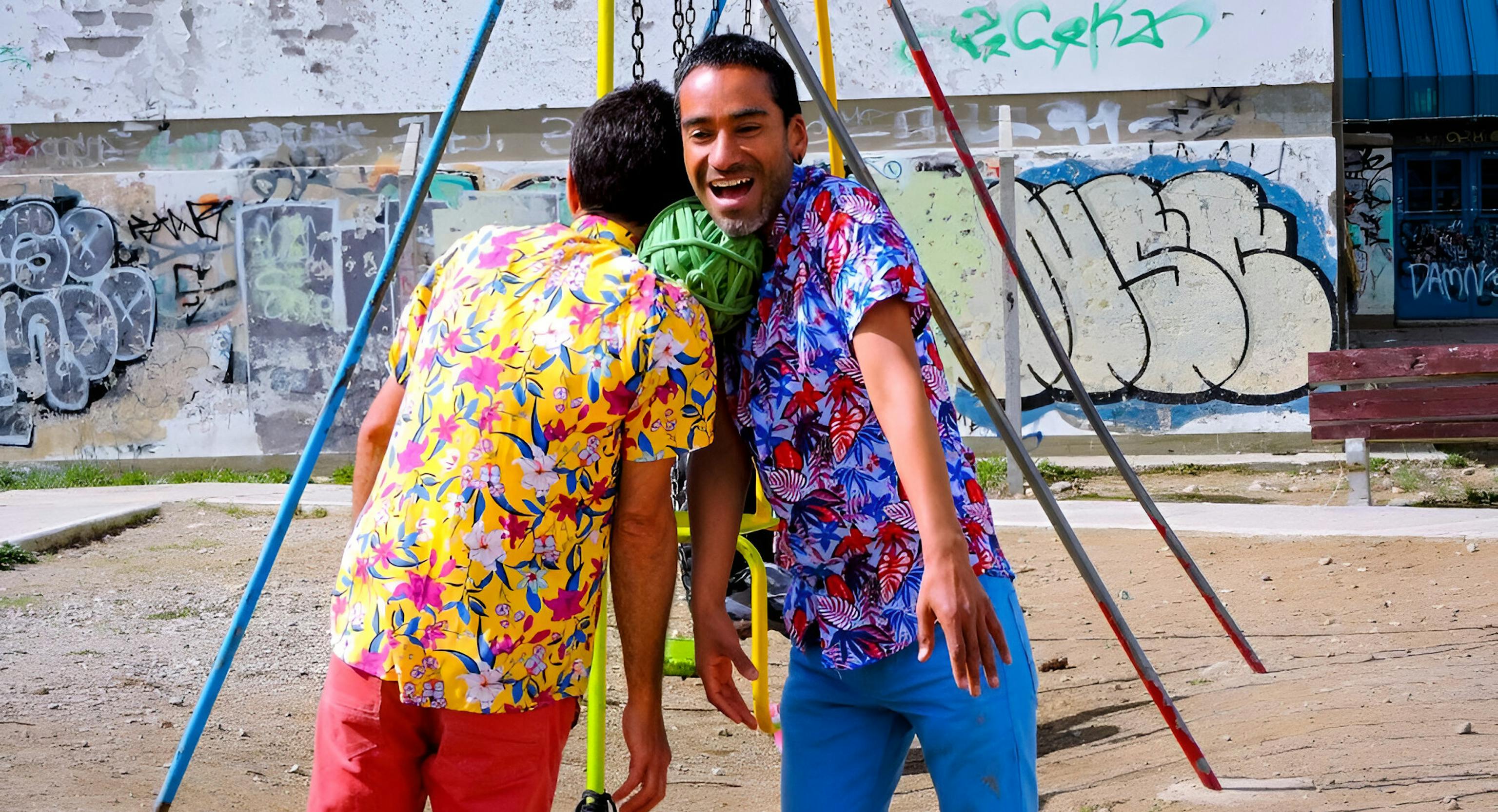 Two performers wearing colourful shirts are holding a ball of rope between with their shoulders