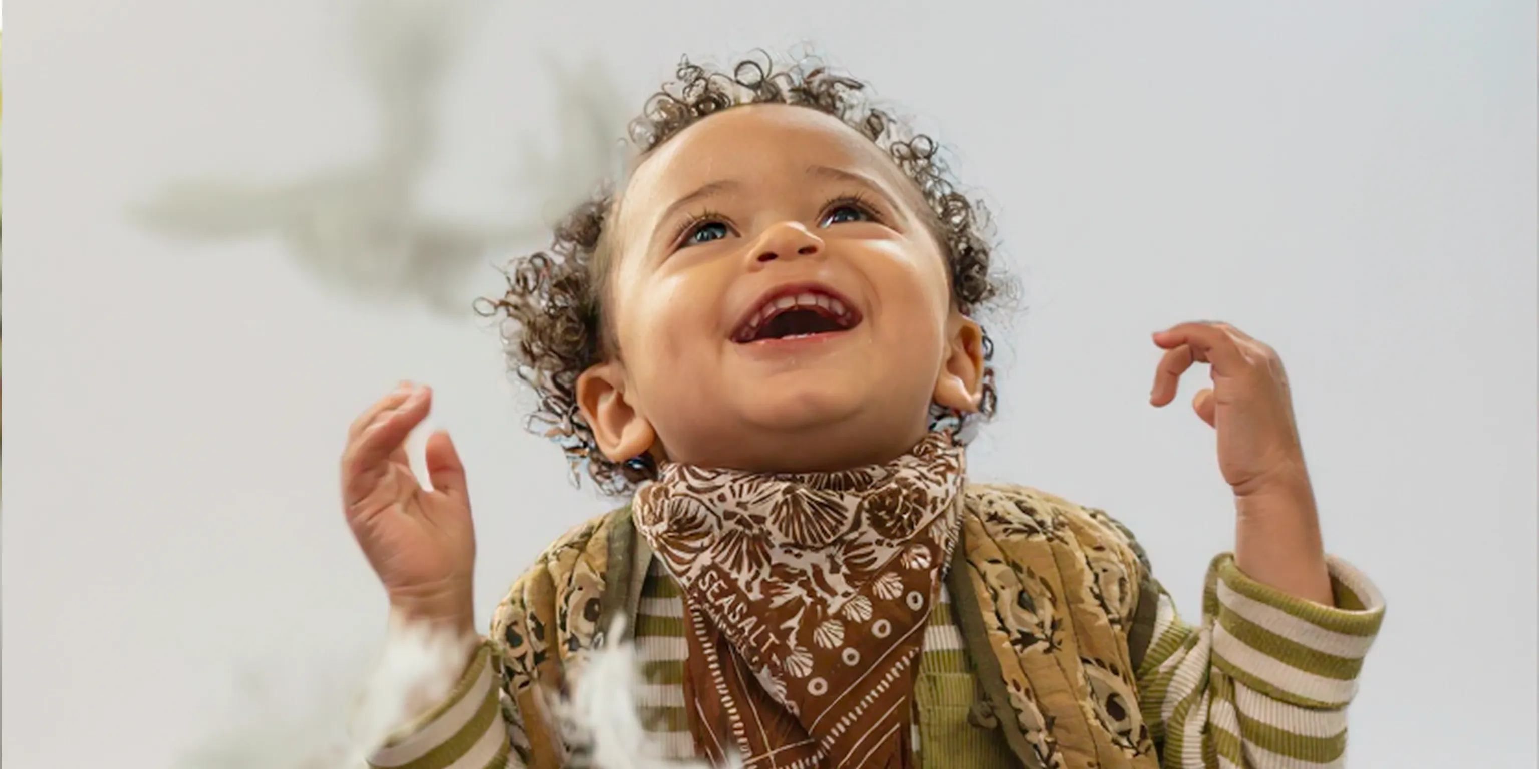 A young child smiling and looking up at feathers cascading down from the sky