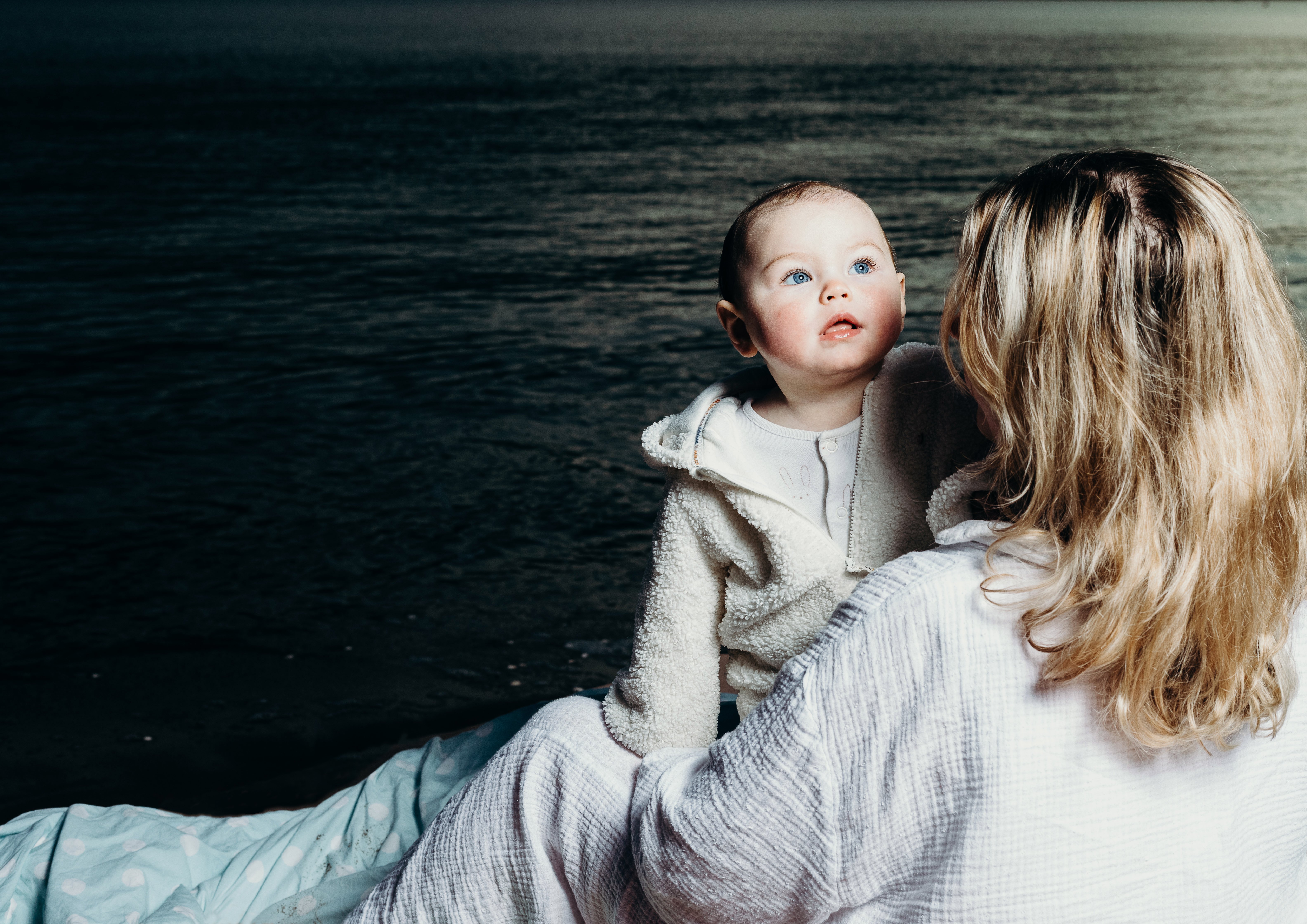 A baby and mother embracing. In the background is the sea