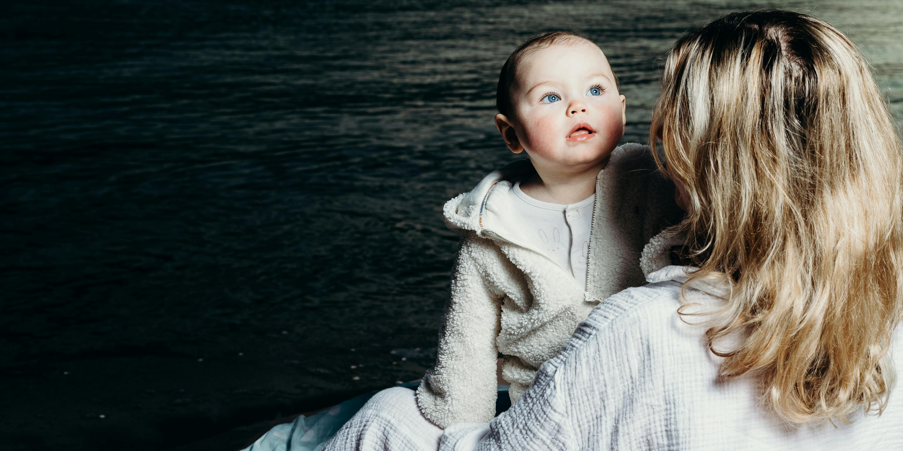 A baby and mother embracing. In the background is the sea