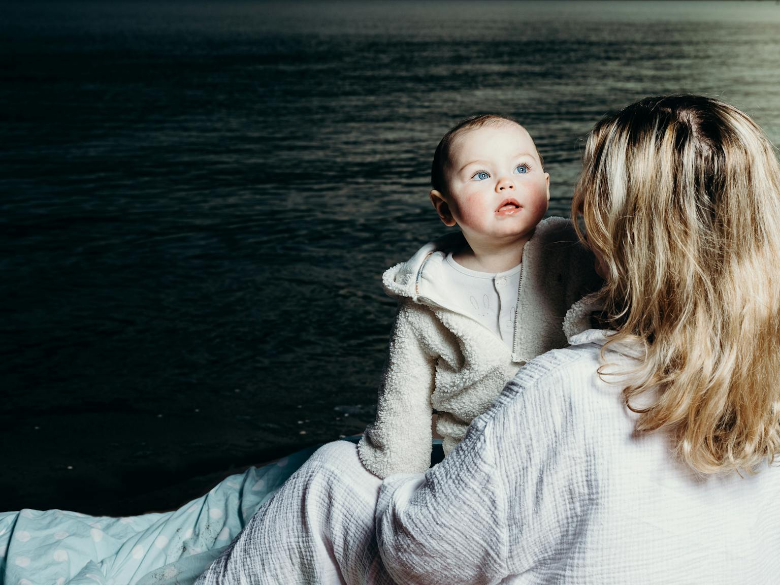 A baby and mother embracing. In the background is the sea
