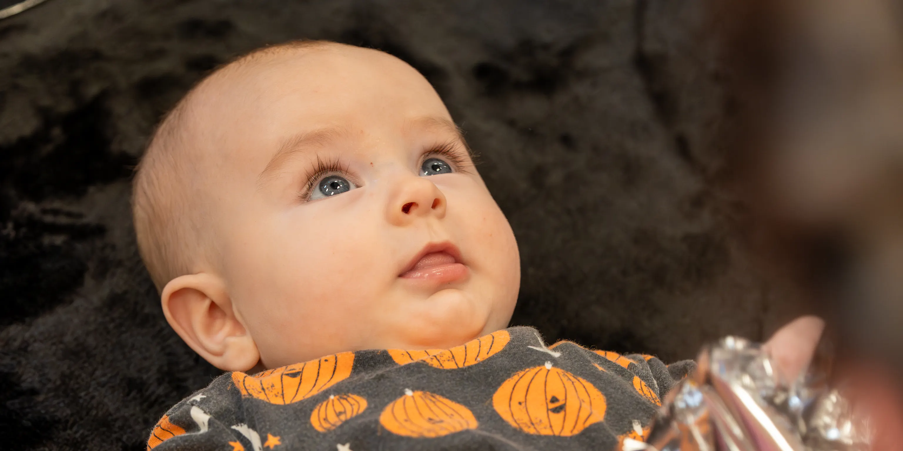 a baby lies on a textured black rug holding a piece of crinkly foil looking up at their parent/carer.