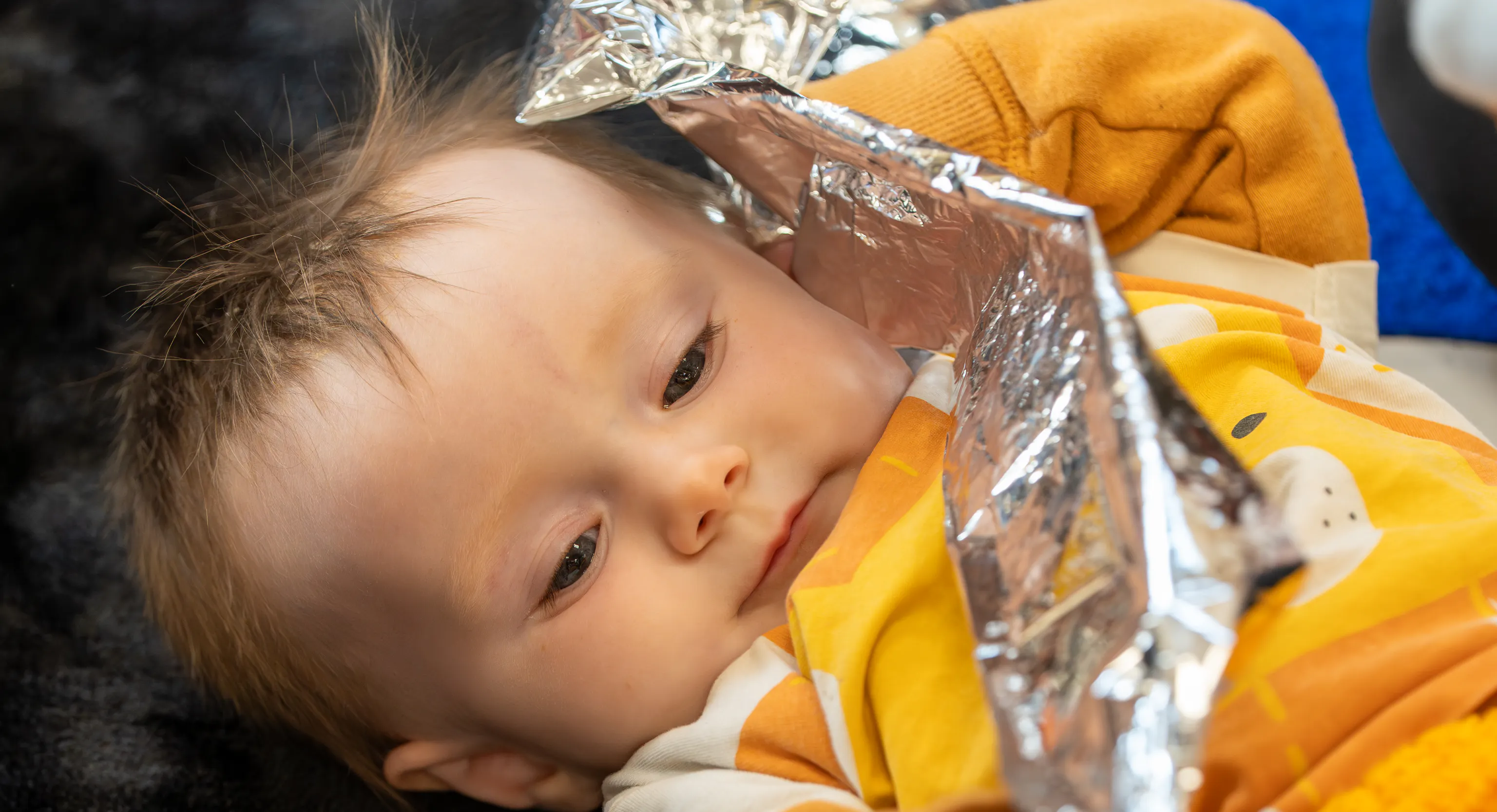 a baby lies on a textured black rug holding a piece of crinkly foil.