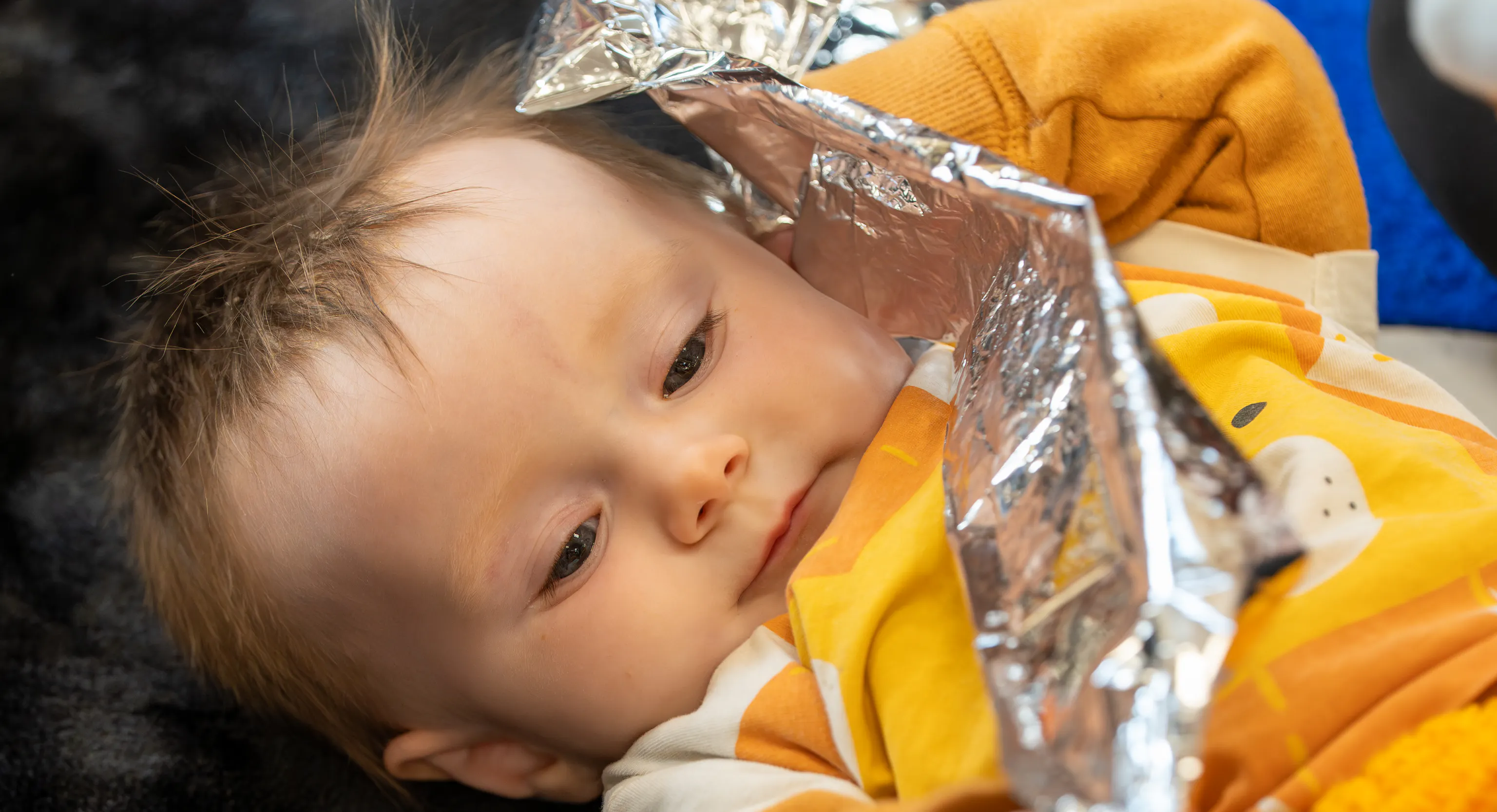 a baby lies on a textured black rug holding a piece of crinkly foil.