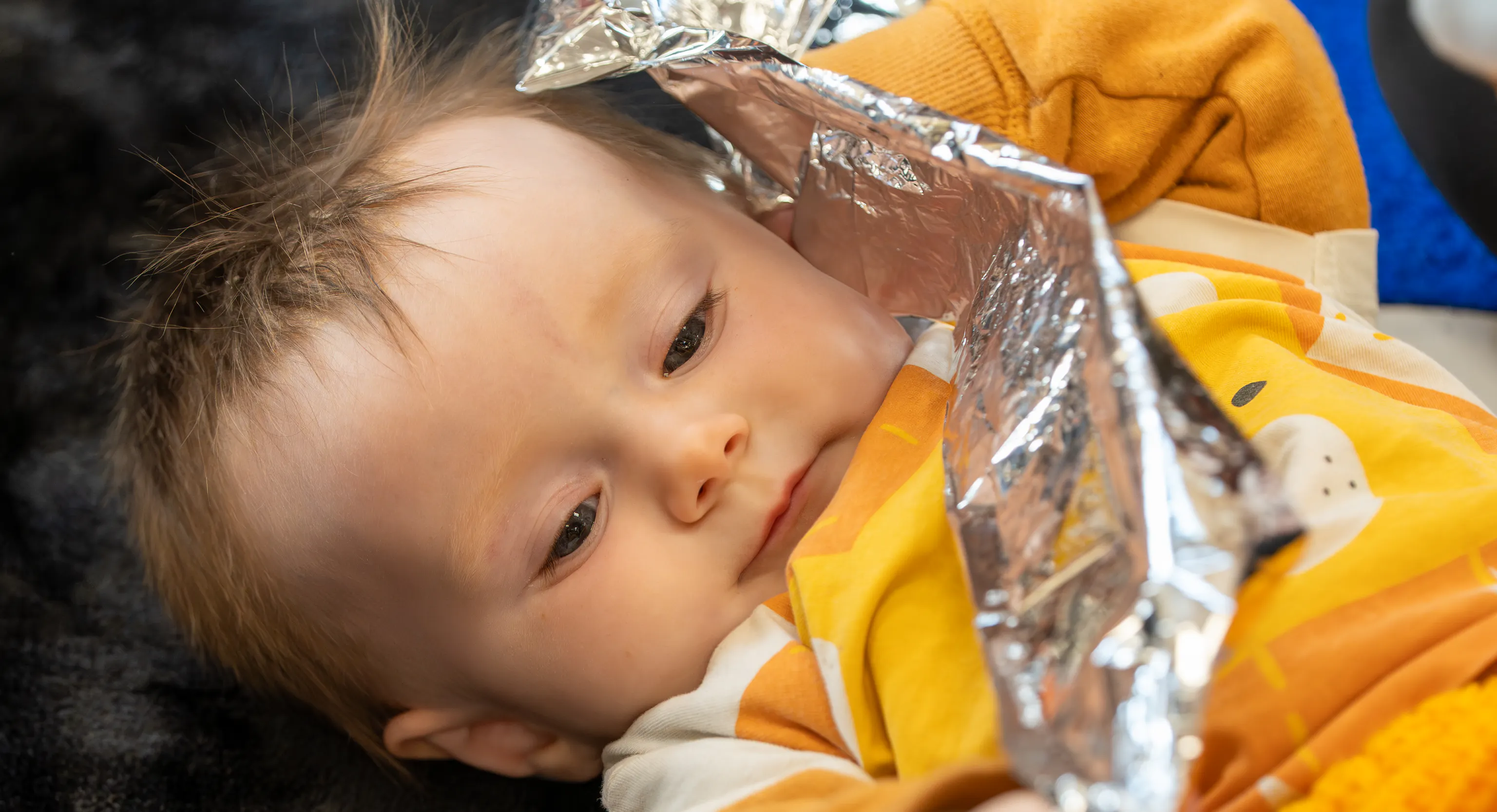a baby lies on a textured black rug holding a piece of crinkly foil.