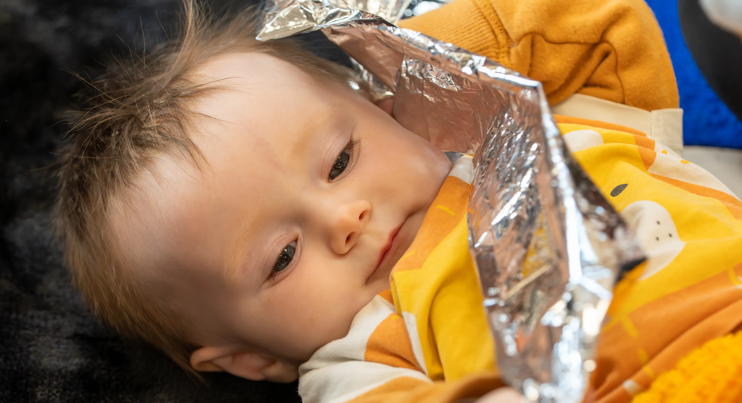 a baby lies on a textured black rug holding a piece of crinkly foil.