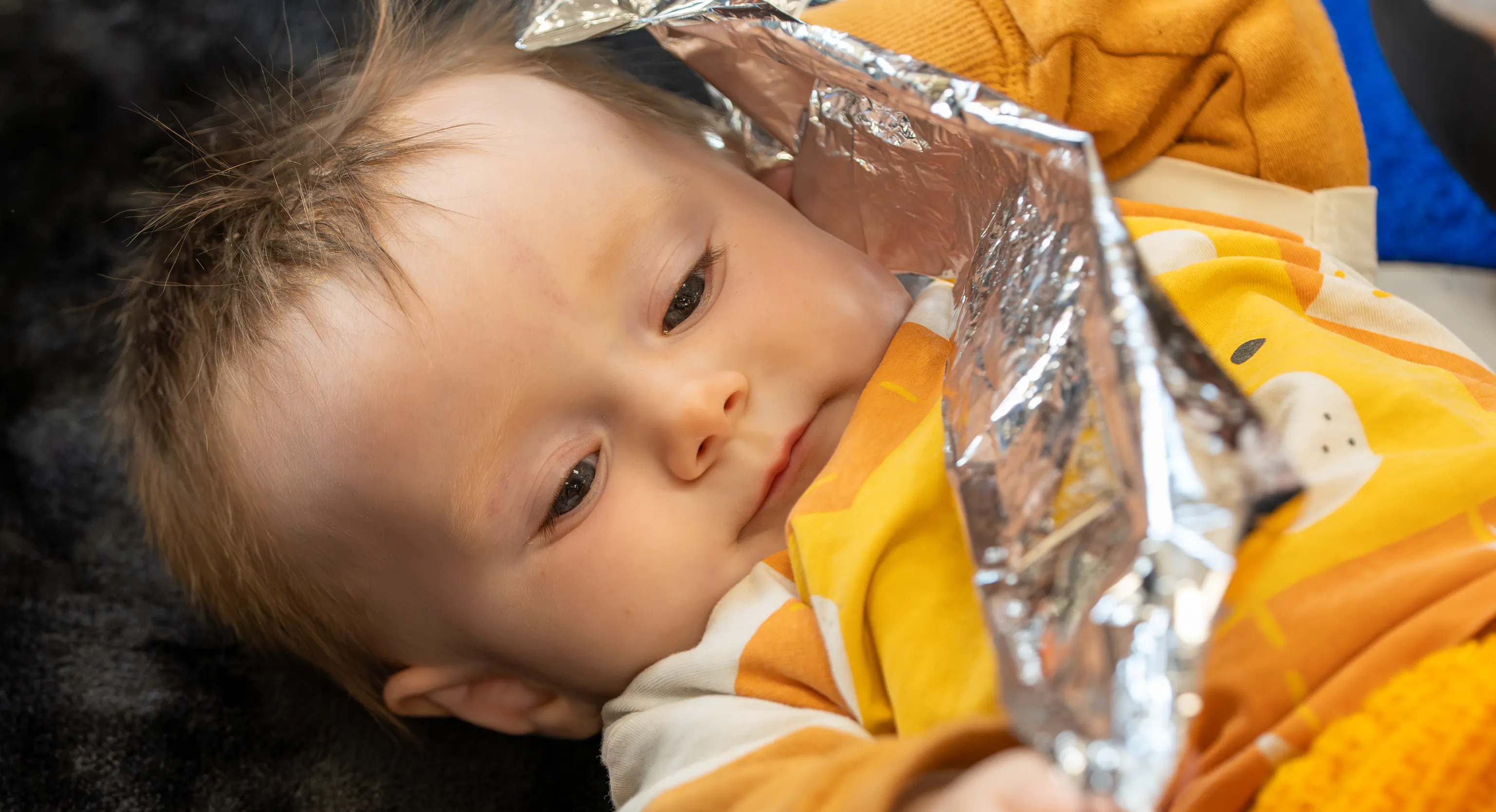a baby lies on a textured black rug holding a piece of crinkly foil.