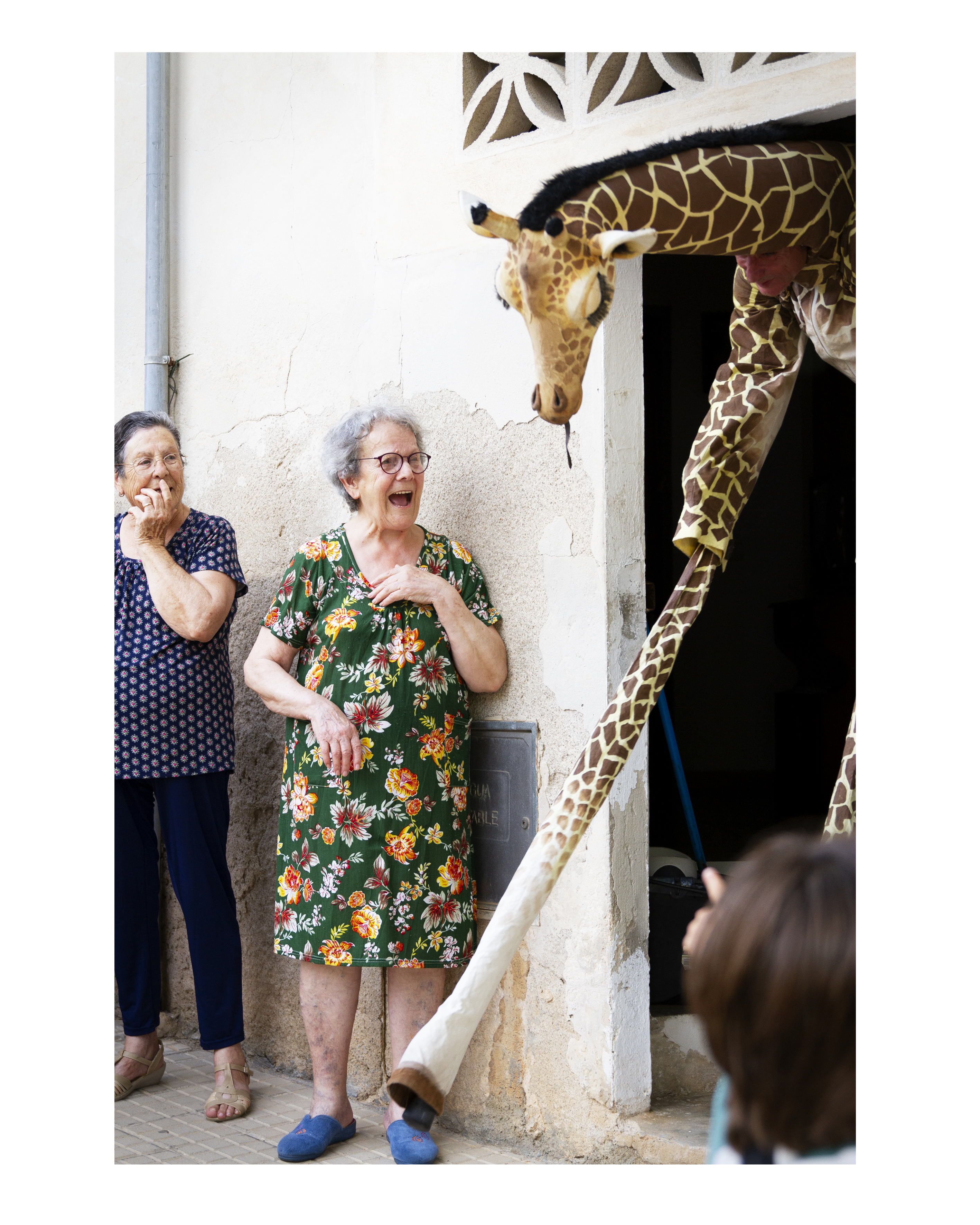 A woman looks surprised at a giraffe coming out of a building 