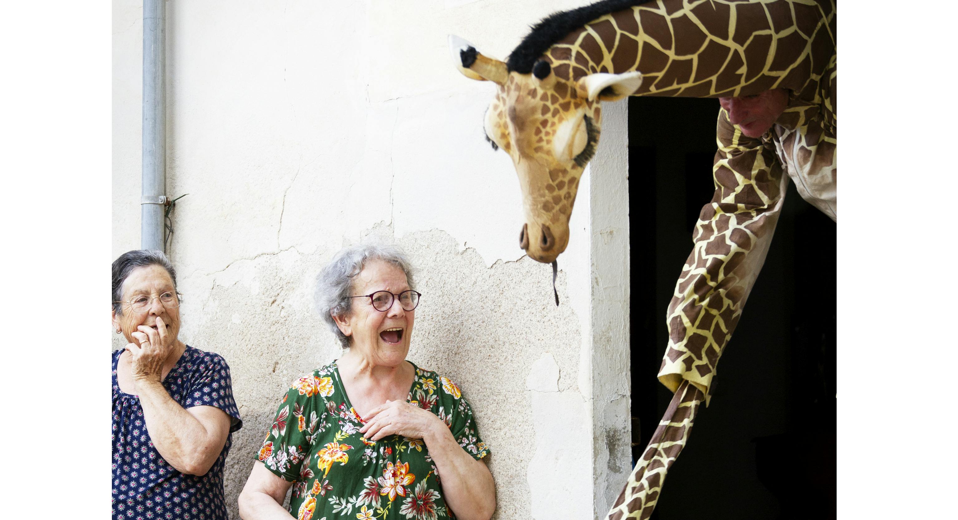 A woman looks surprised at a giraffe coming out of a building