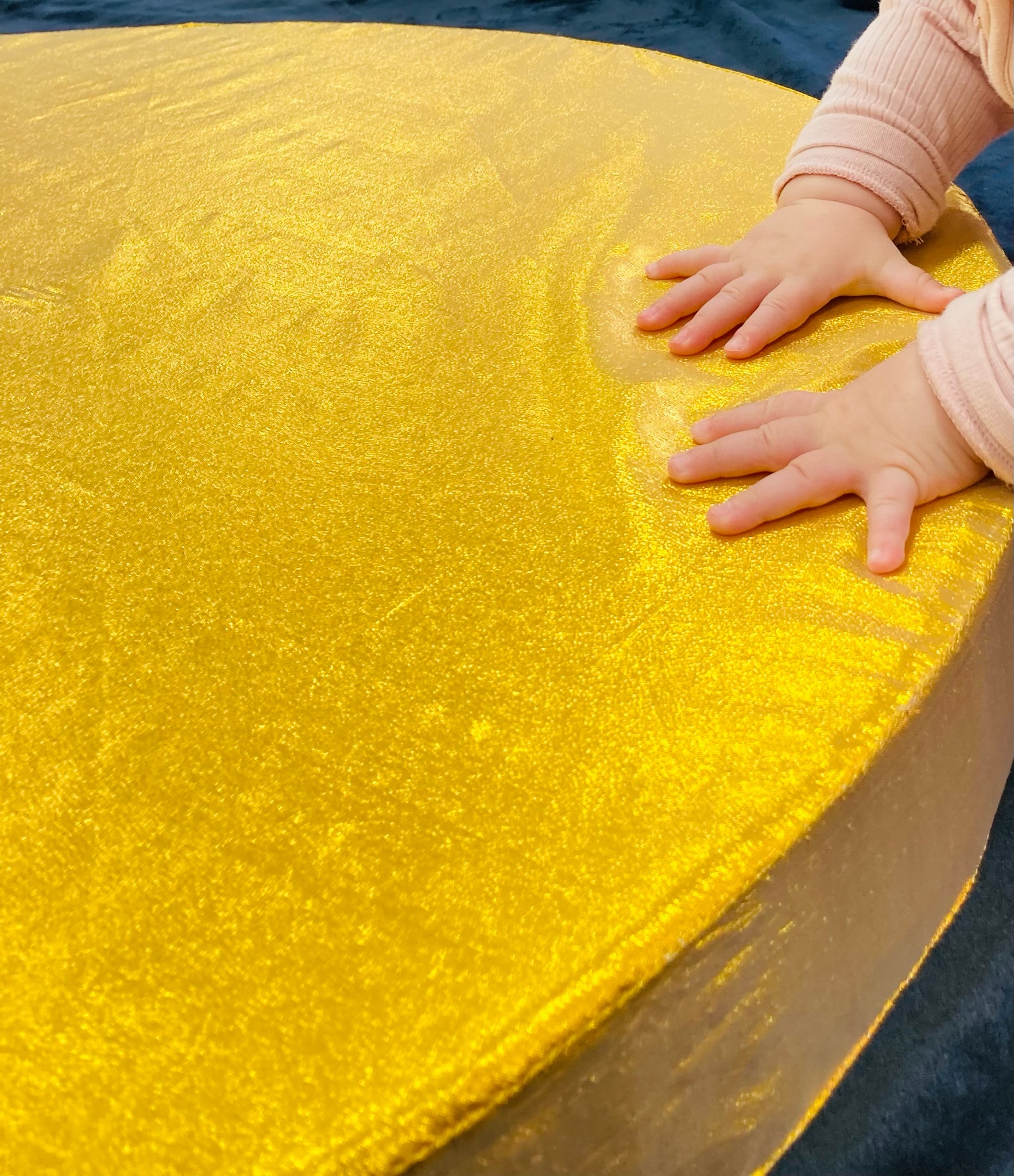 A baby touching a golden piece on material 