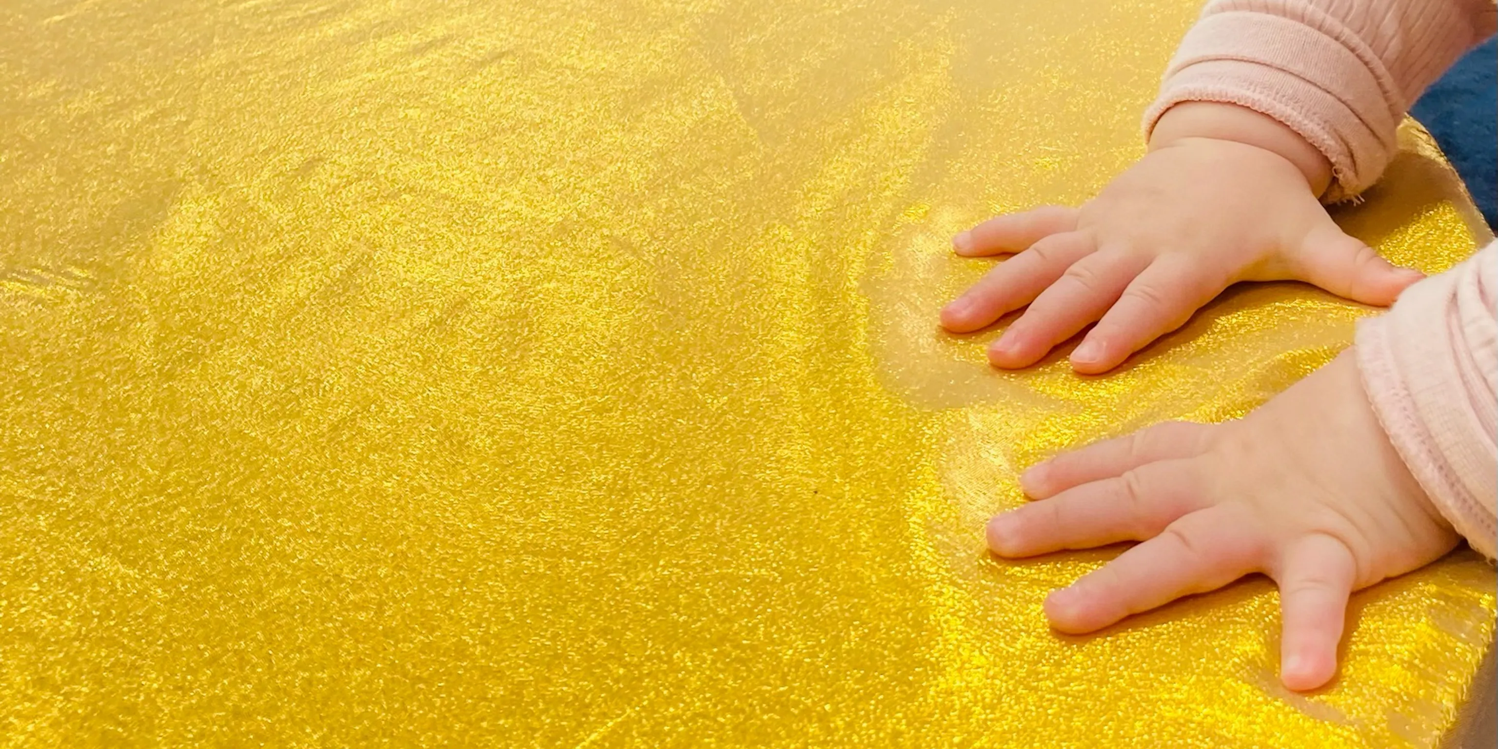 A baby touching a golden piece on material