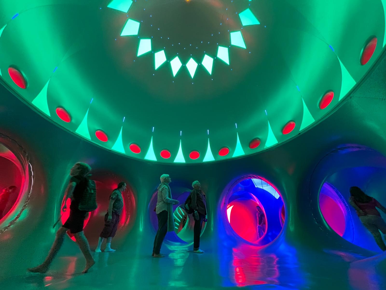 Adults and young children stood inside of a dome structure with red, green, pink and blue lights
