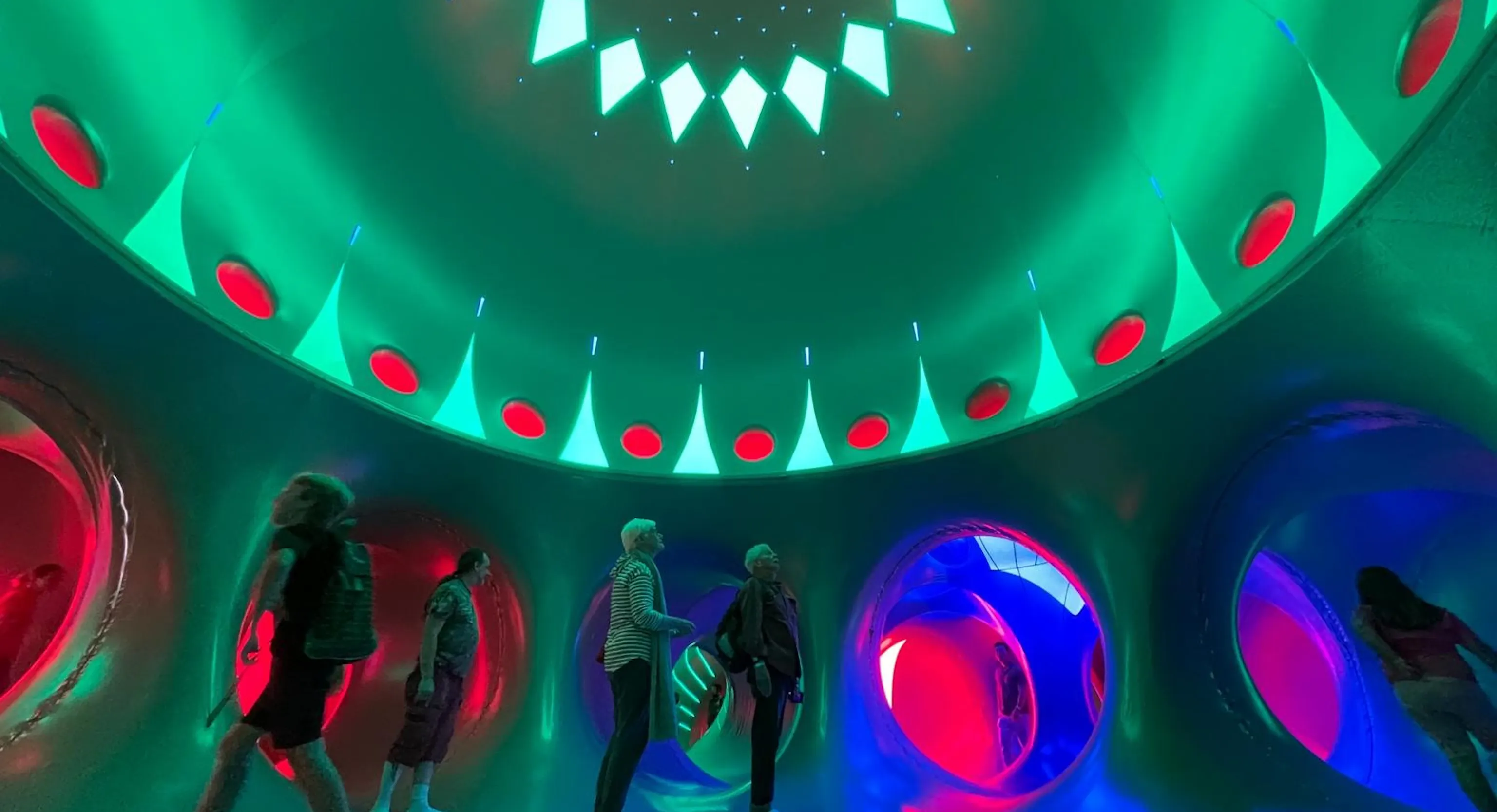 Adults and young children stood inside of a dome structure with red, green, pink and blue lights