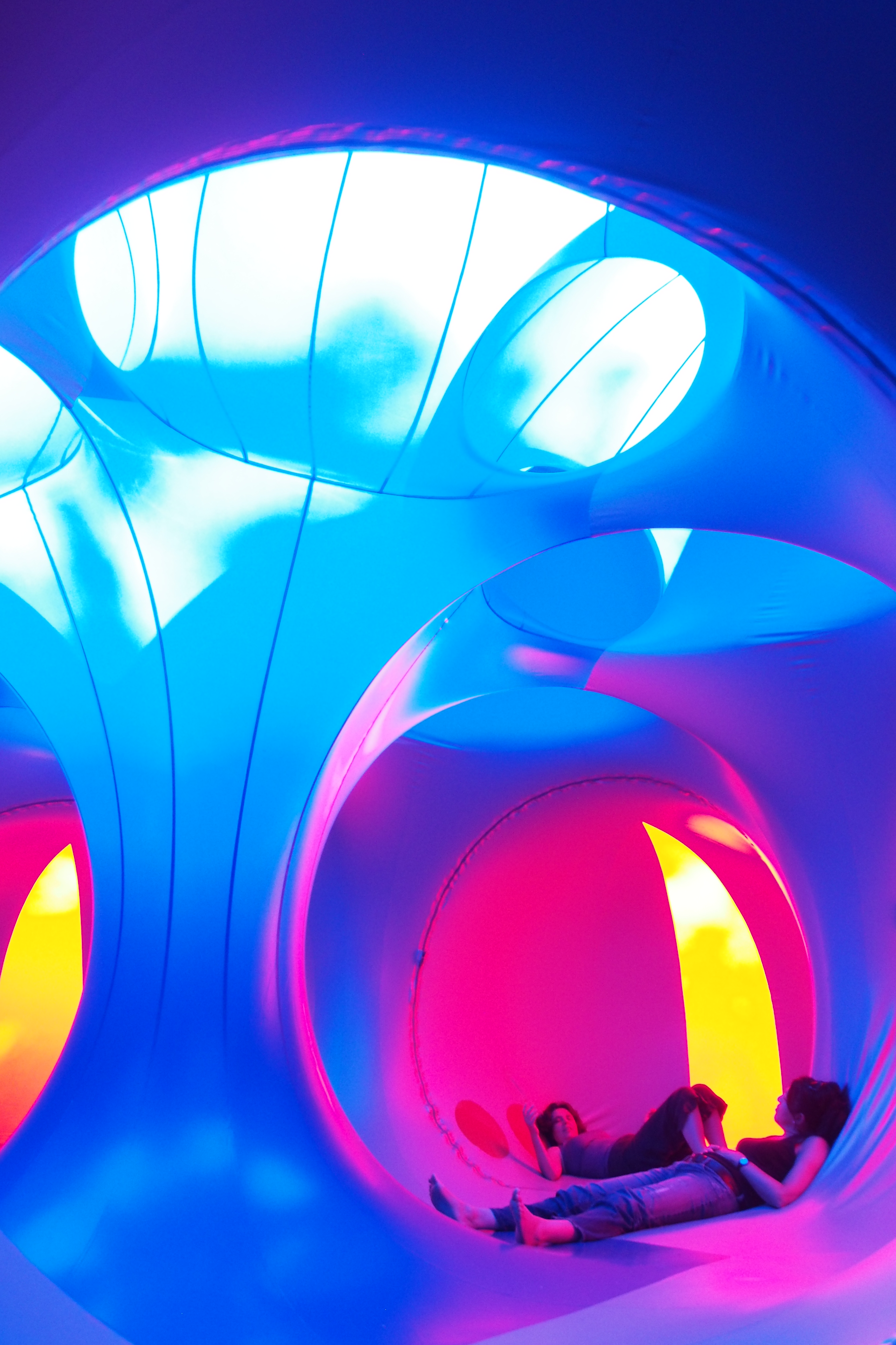 An adult and young child lying on the ground inside of a dome structure with yellow, pink and blue lights
