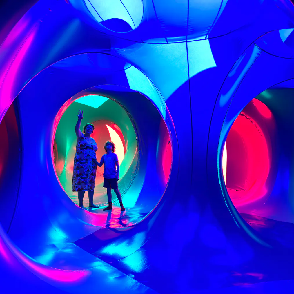 An adult and young child stood inside of a dome structure with red, yellow, pink and blue lights