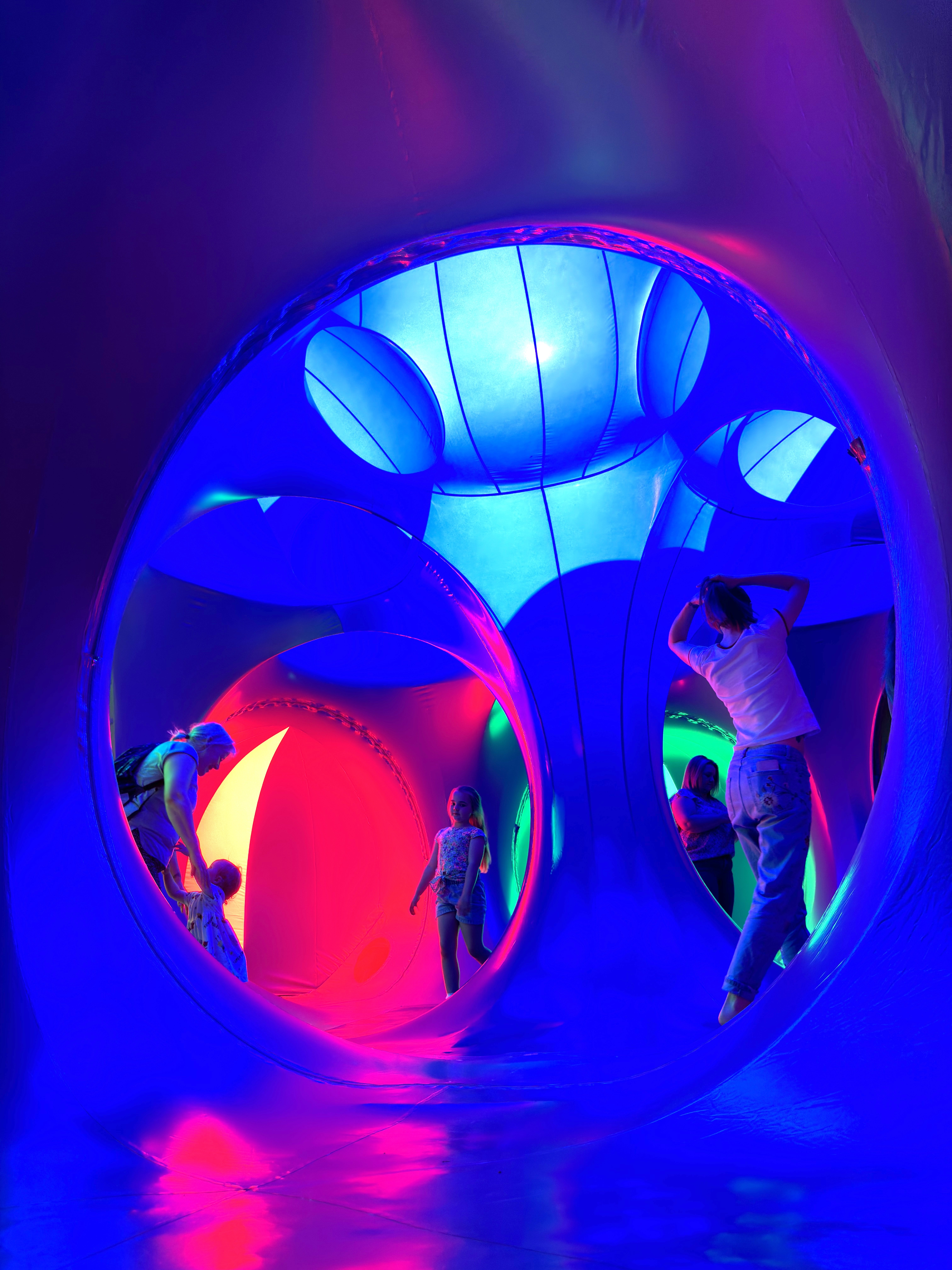 Adults and young children stood inside of a dome structure with pink and blue lights