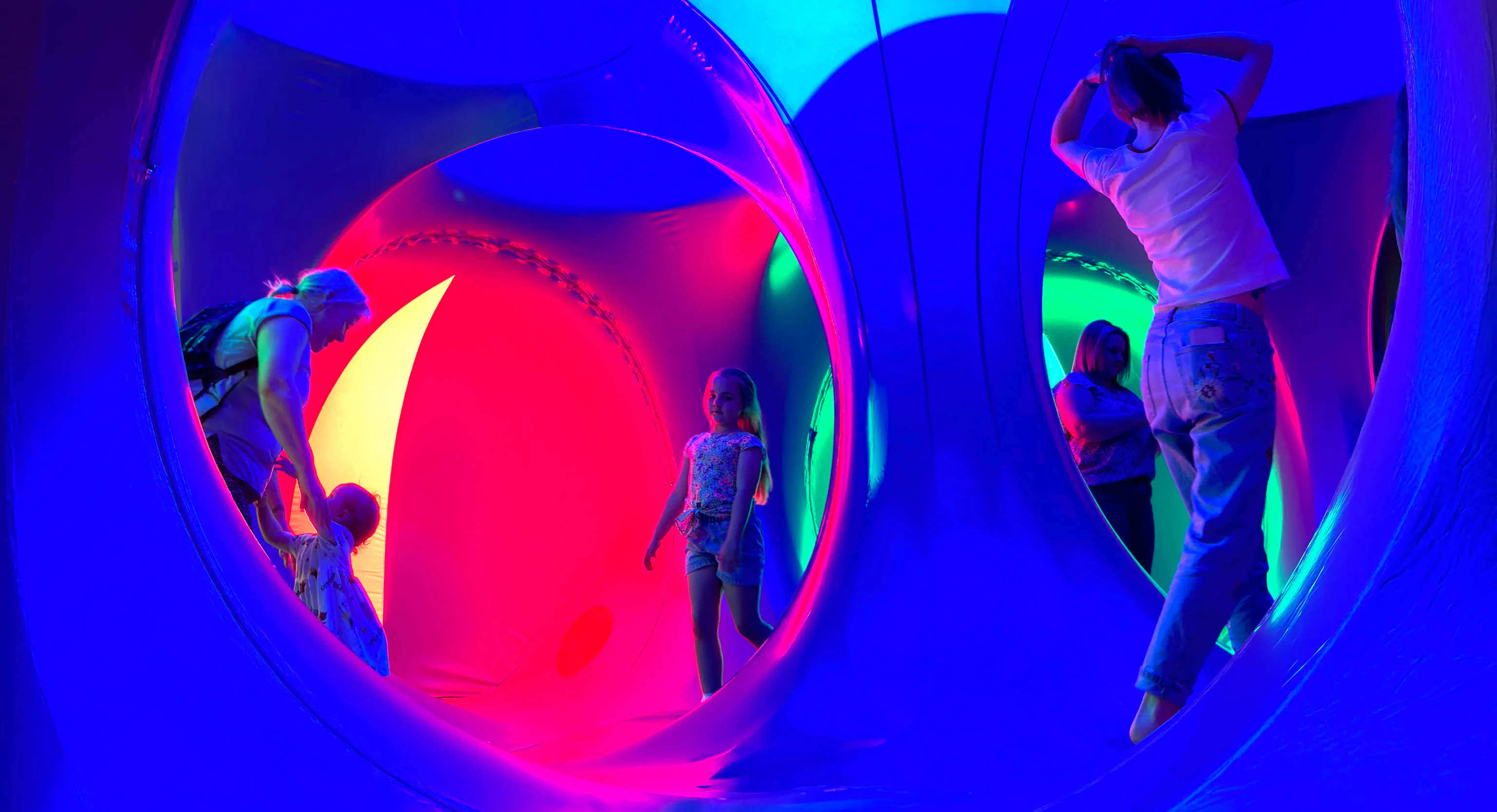 Adults and young children stood inside of a dome structure with pink and blue lights