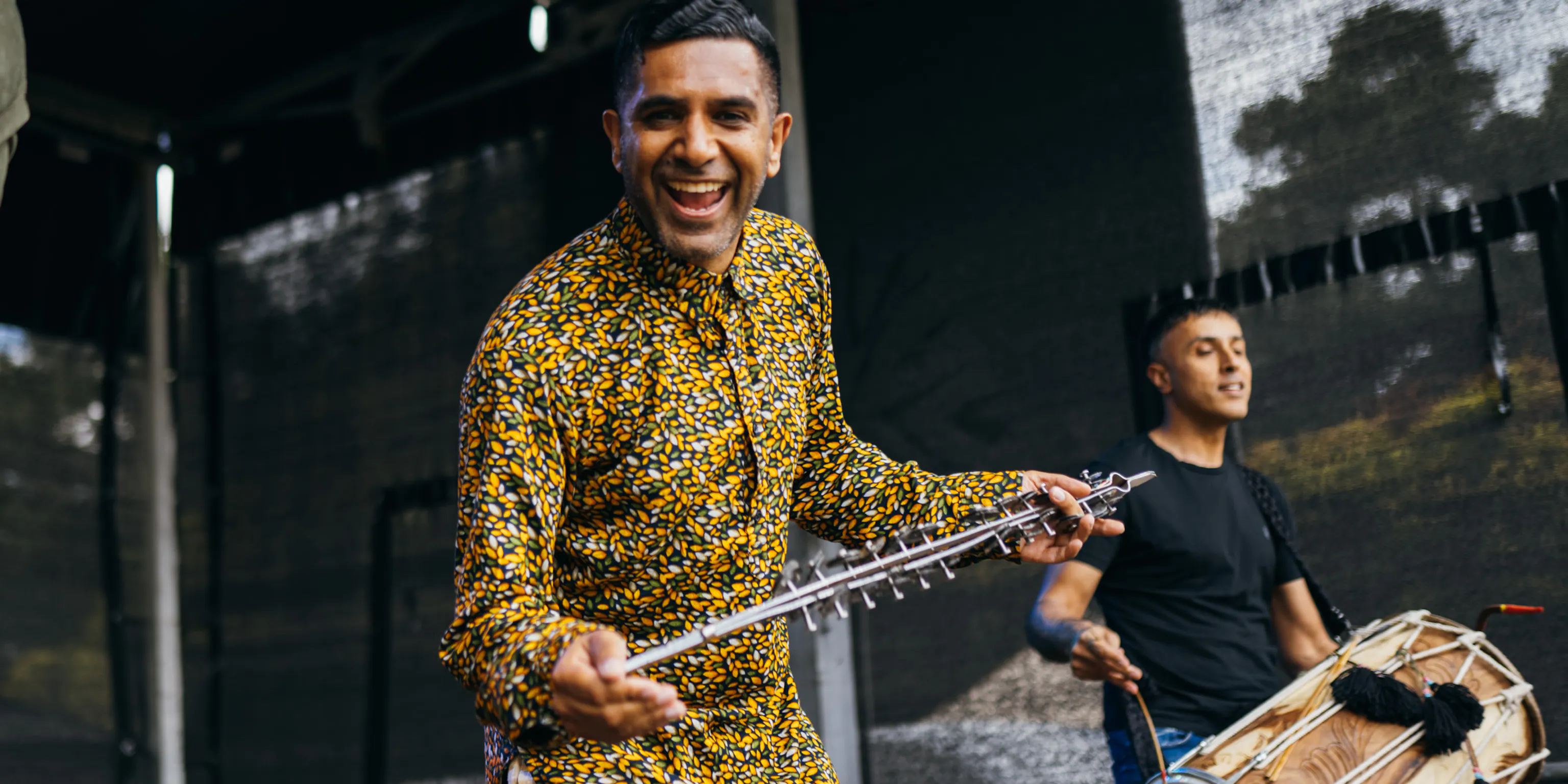 An artist smiling at the camera whilst holding an instrument
