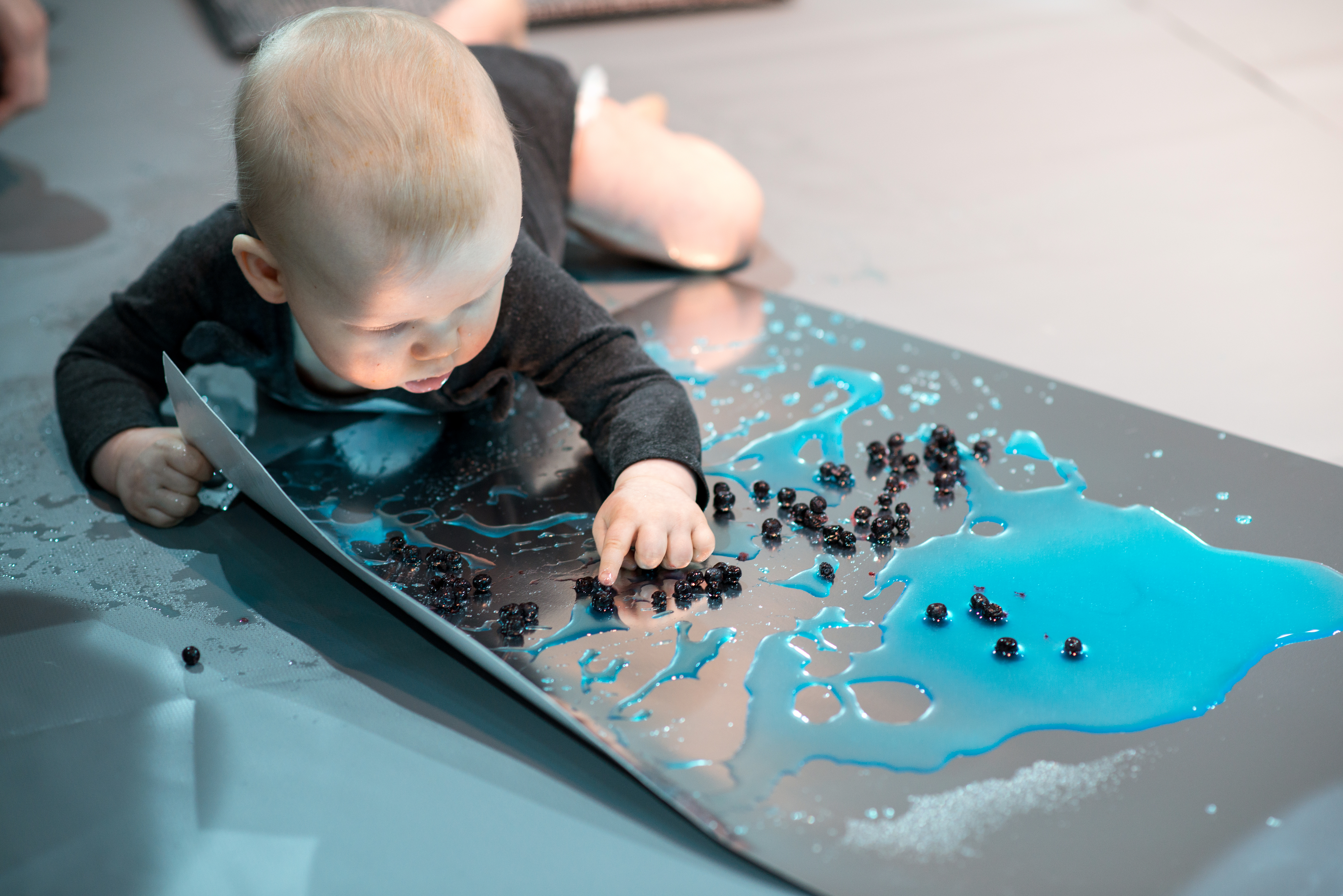Colour Workshops: a baby lying on their front and playing with blue colours and small black shapes