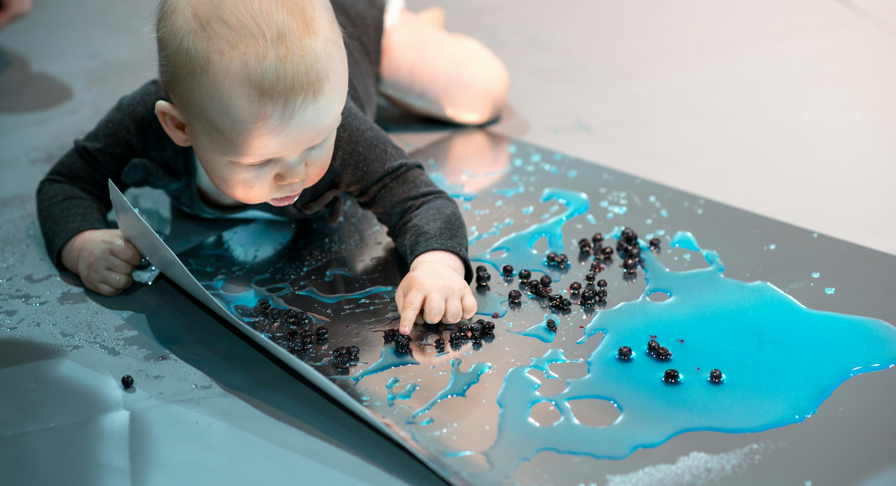 Colour Workshops: a baby lying on their front and playing with blue colours and small black shapes