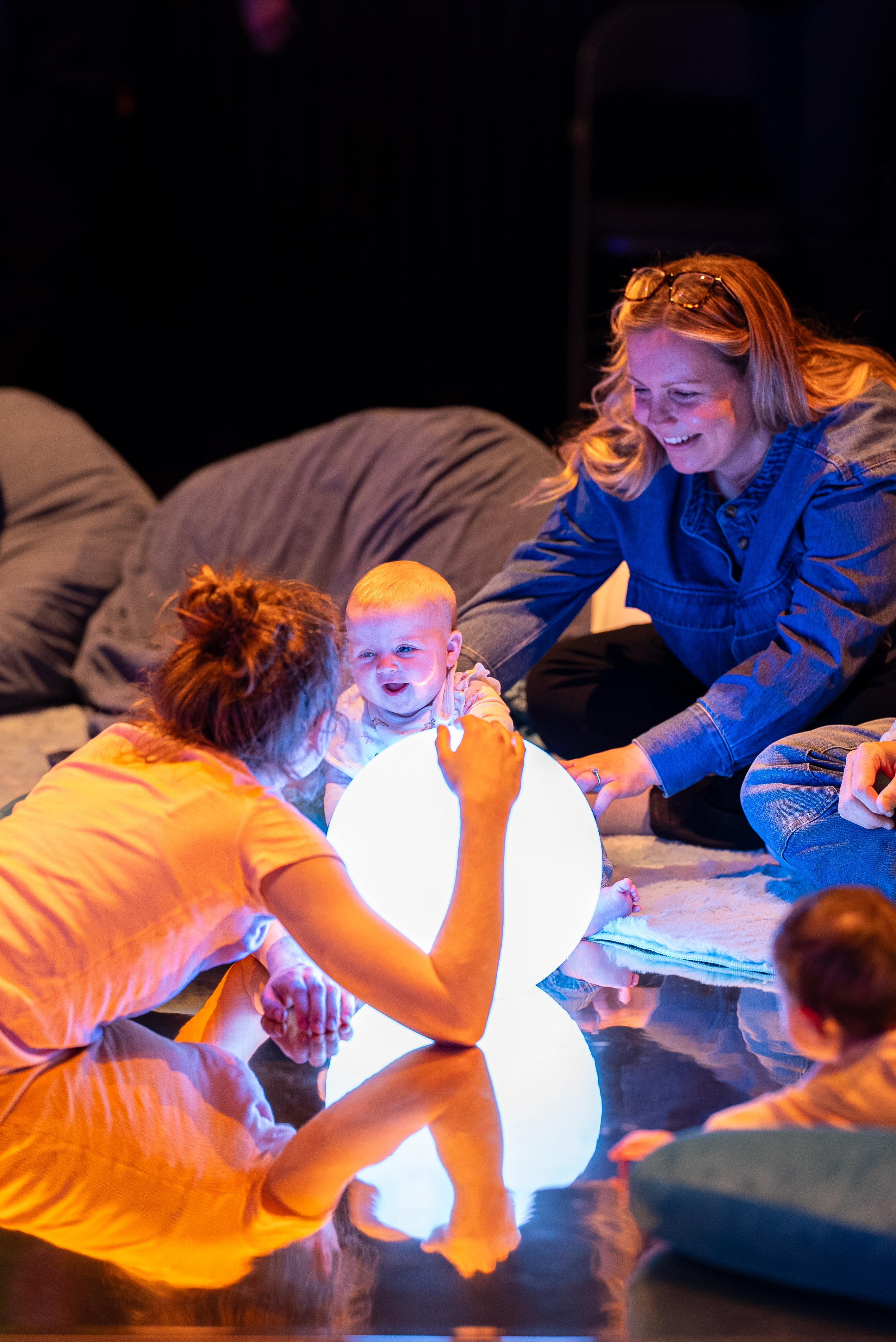 Parent / carer and baby engaging with big spherical light. Both are smiling.